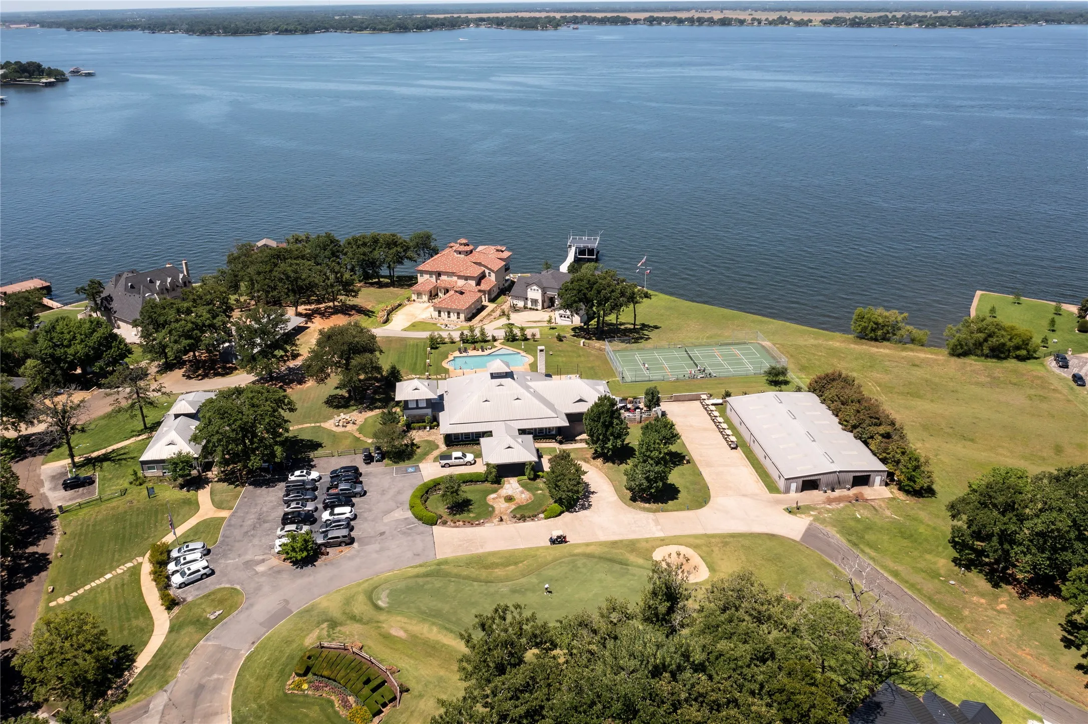 Expansive property featuring a waterfront setting, private tennis courts, an in-ground swimming pool, a golf course putting green, and a large multi-vehicle parking area