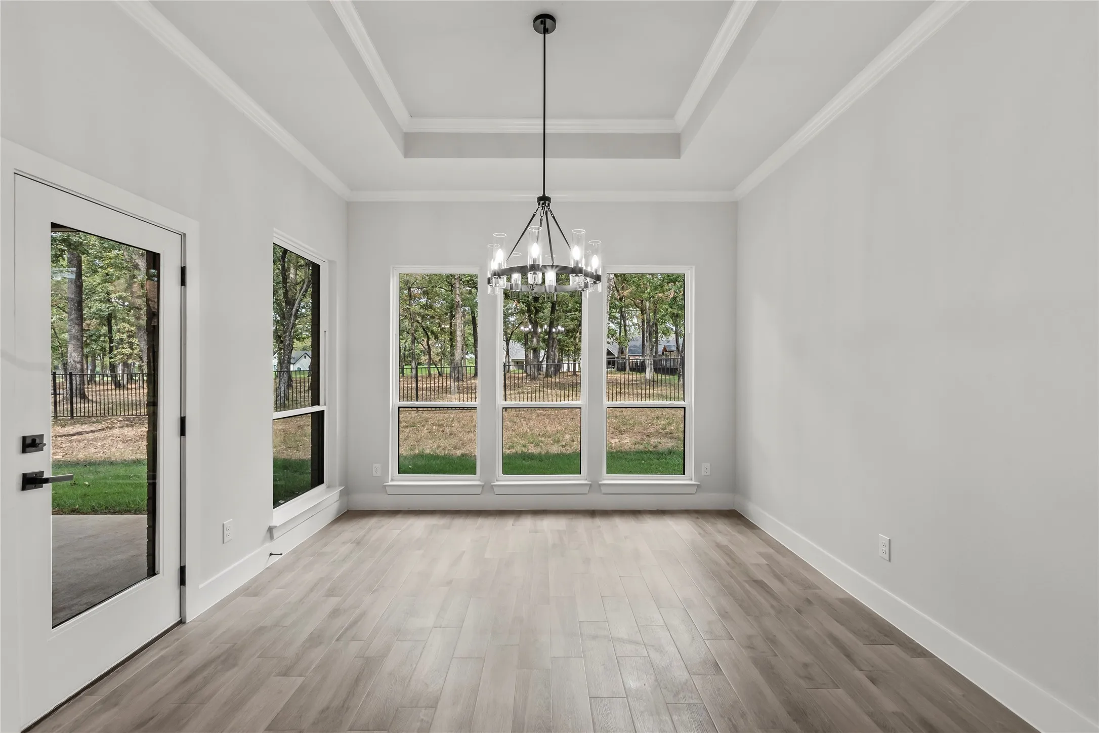 Tray ceiling with crown molding, wood-finish flooring, full-light exterior door, triple pane windows, and a contemporary chandelier