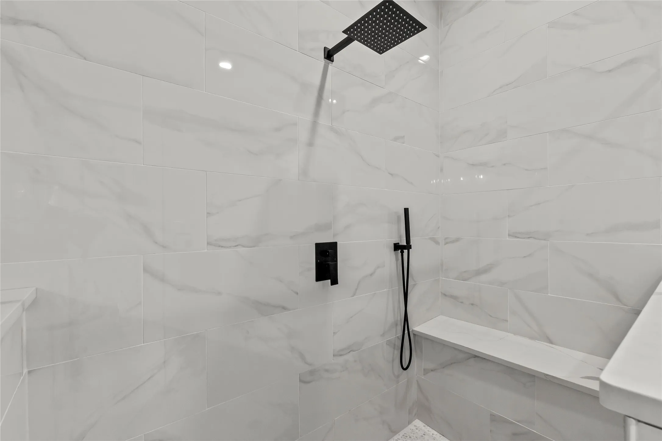Tiled shower with a rainfall showerhead, handheld sprayer, and built-in bench