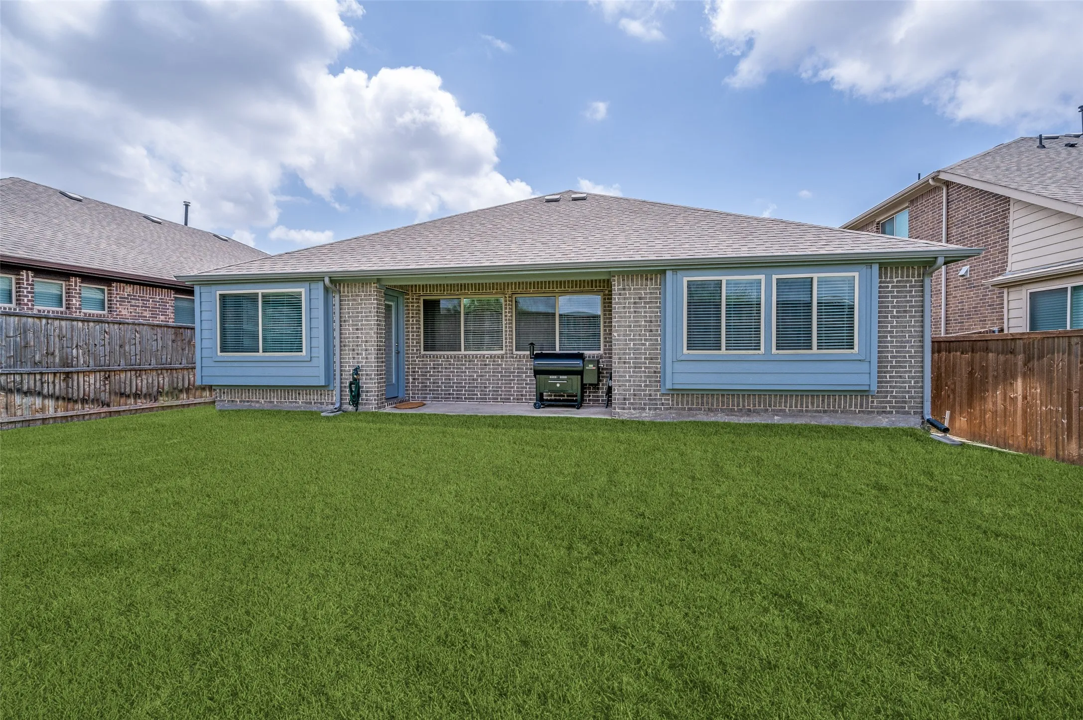 Expansive green lawn with a brick exterior, grey shingle roof, and multiple large windows