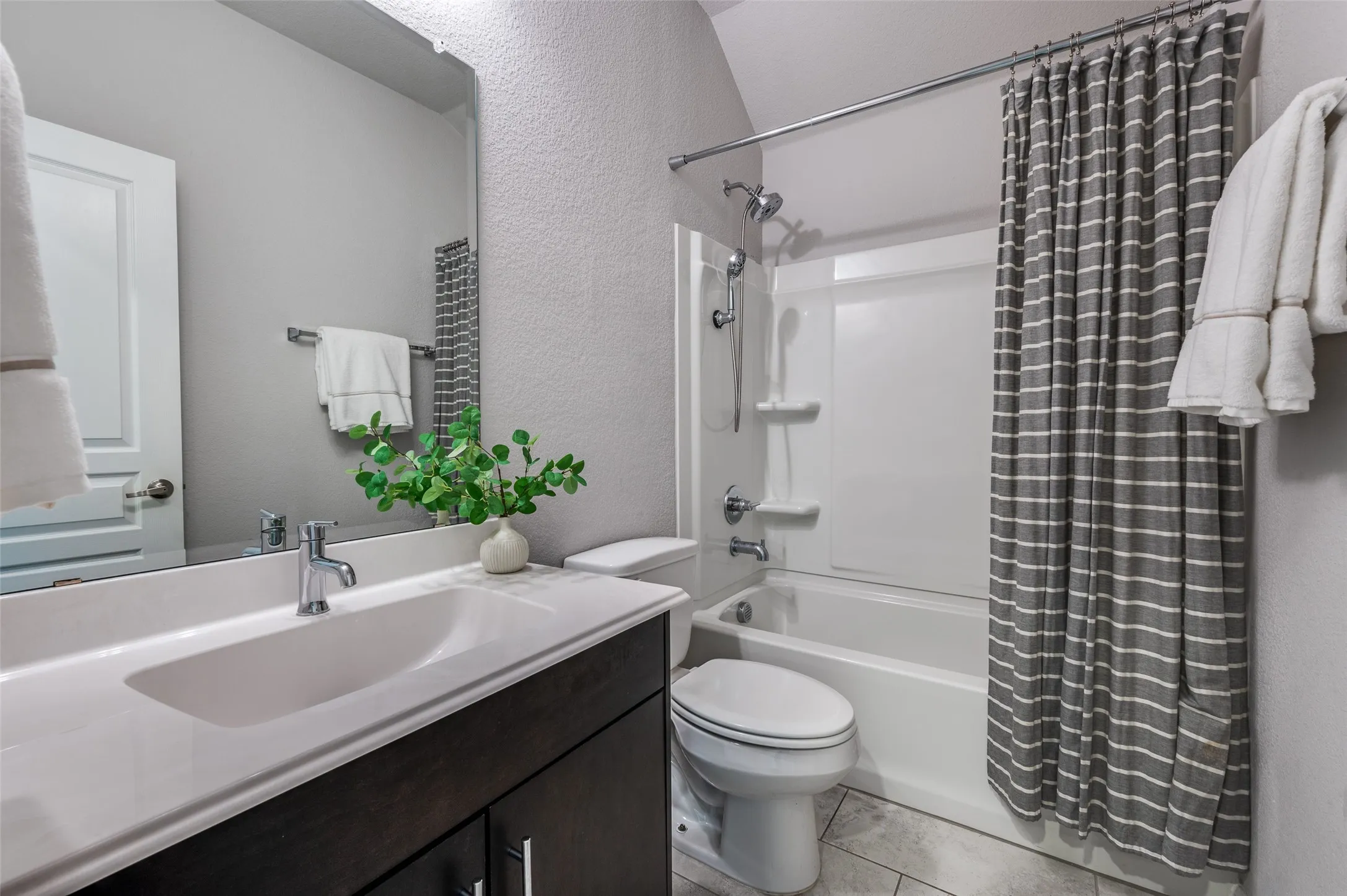 Bathroom featuring a single vanity with integrated sink, dark wood-finish cabinetry, a large wall mirror, and a white tub/shower combination