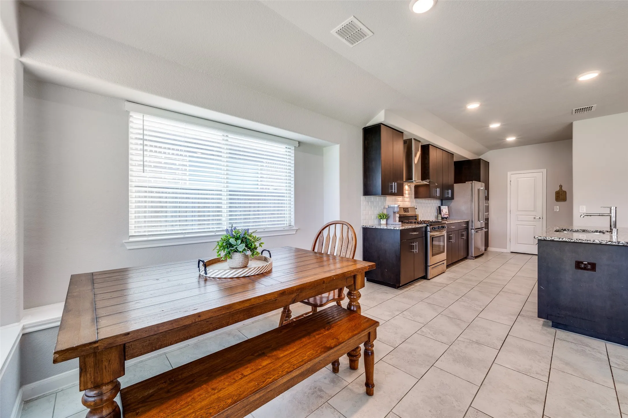 Kitchen featuring dark wood-finish cabinetry, stainless steel appliances, speckled stone countertops, a tiled backsplash, and recessed lighting