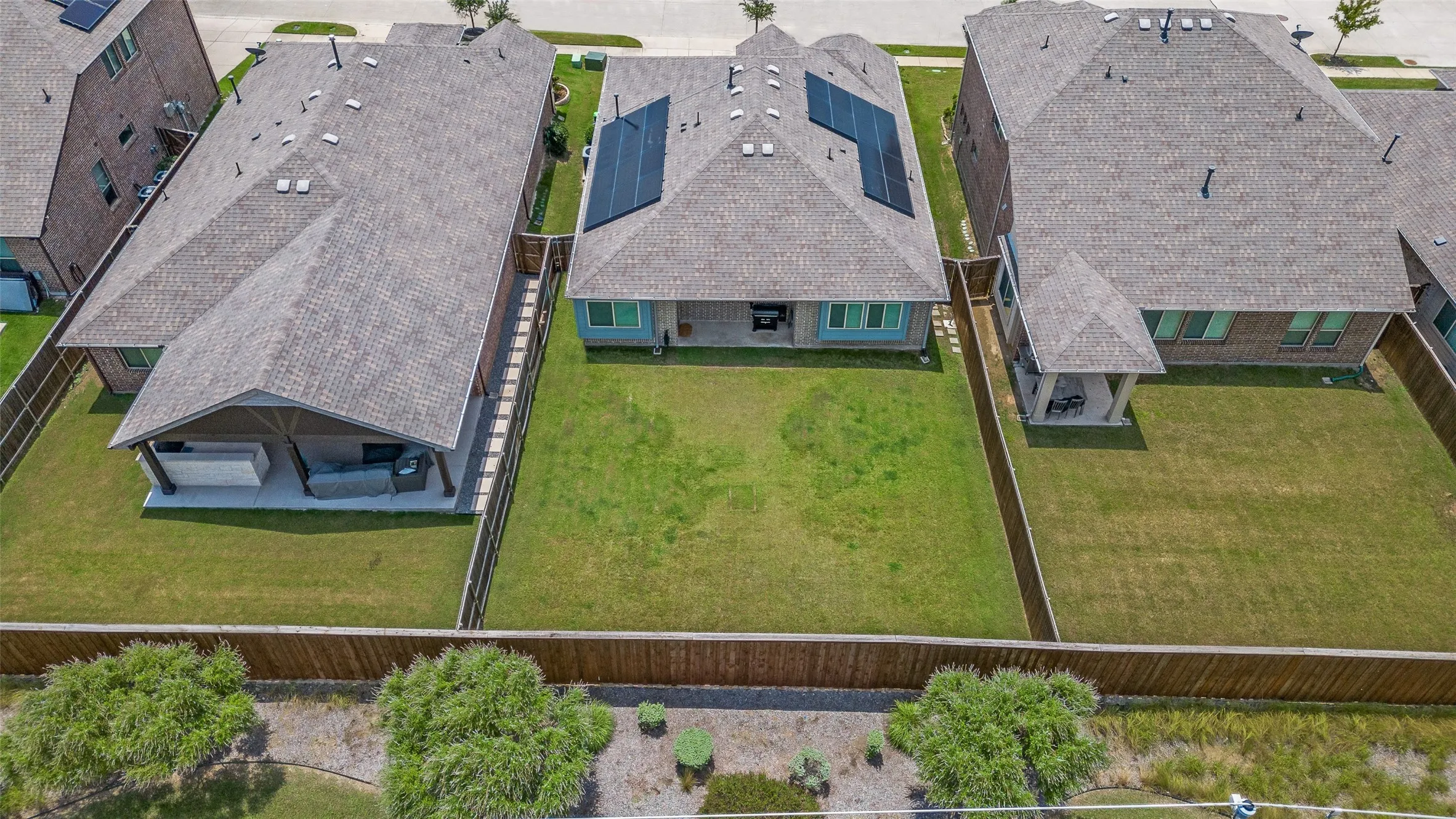 Gable roofline, solar panel installation, rear yard with lawn, covered patio, and wood privacy fencing