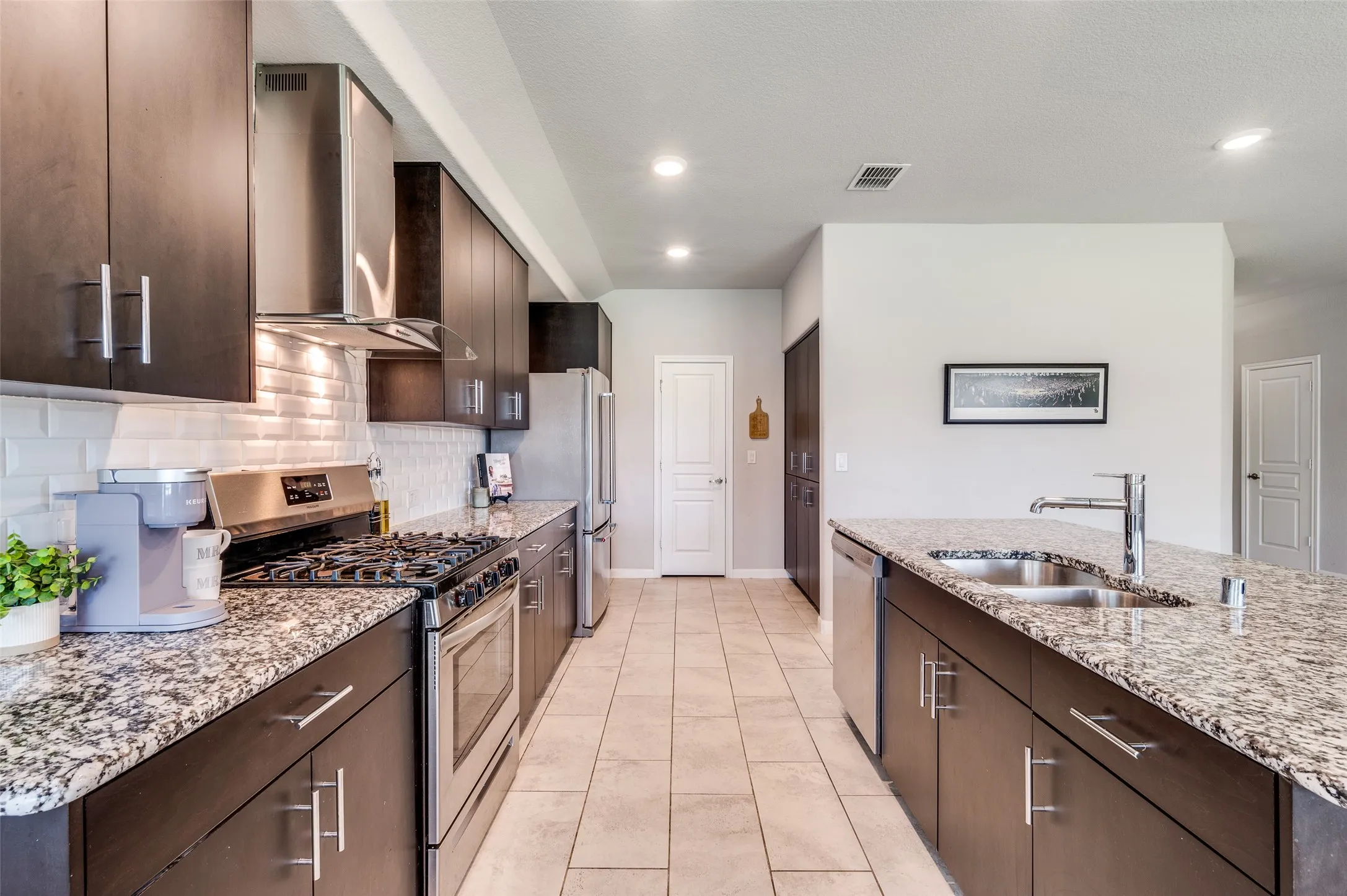 Contemporary kitchen featuring dark wood-finish cabinetry, light-toned tile flooring, and stainless steel appliances