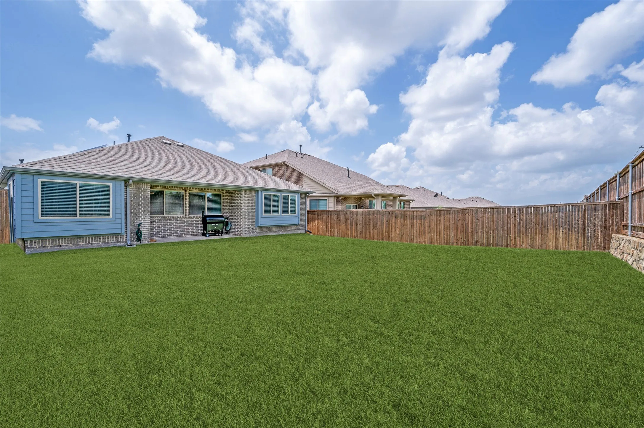 Expansive green lawn, wood fence perimeter, covered patio, multiple windows, and a shingle roof