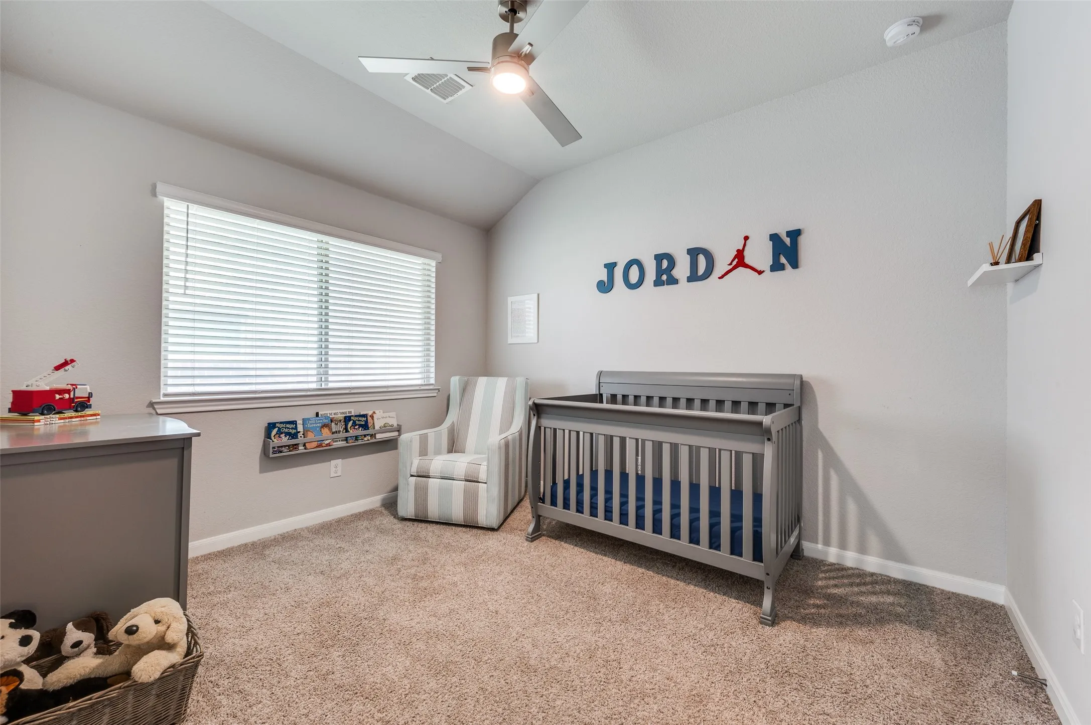 Carpeted flooring, vaulted ceiling, ceiling fan, window with blinds, and built-in shelving