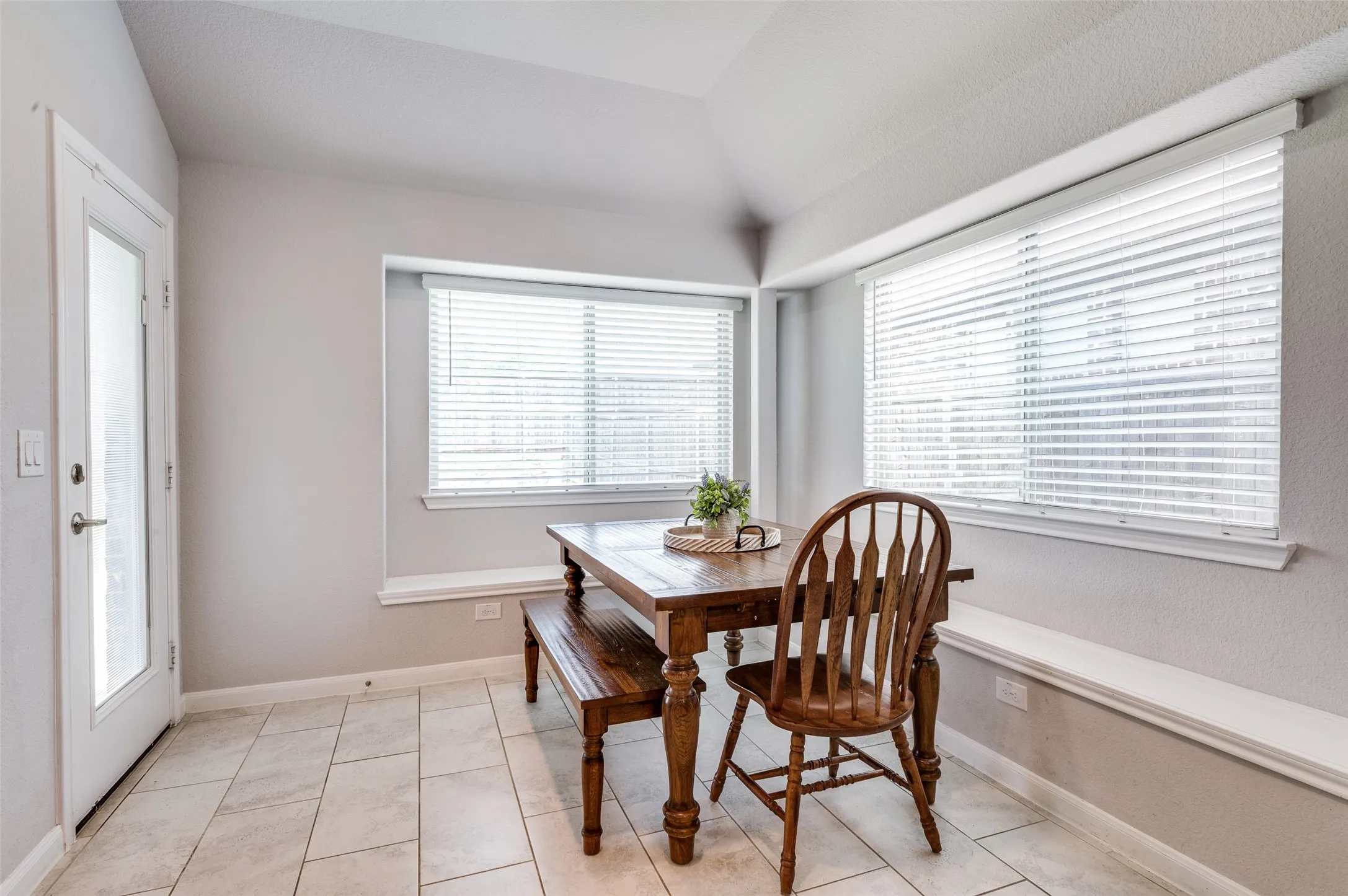Vaulted ceiling, tiled flooring, built-in window seating, and multiple windows with blinds