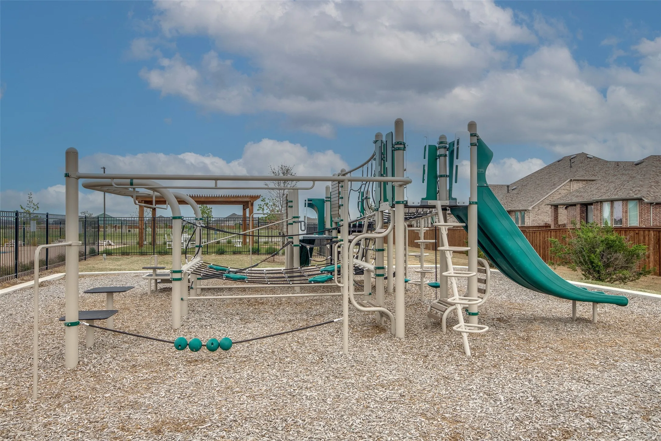 Playground structure featuring a slide, climbing elements, and monkey bars, set on a wood chip surface