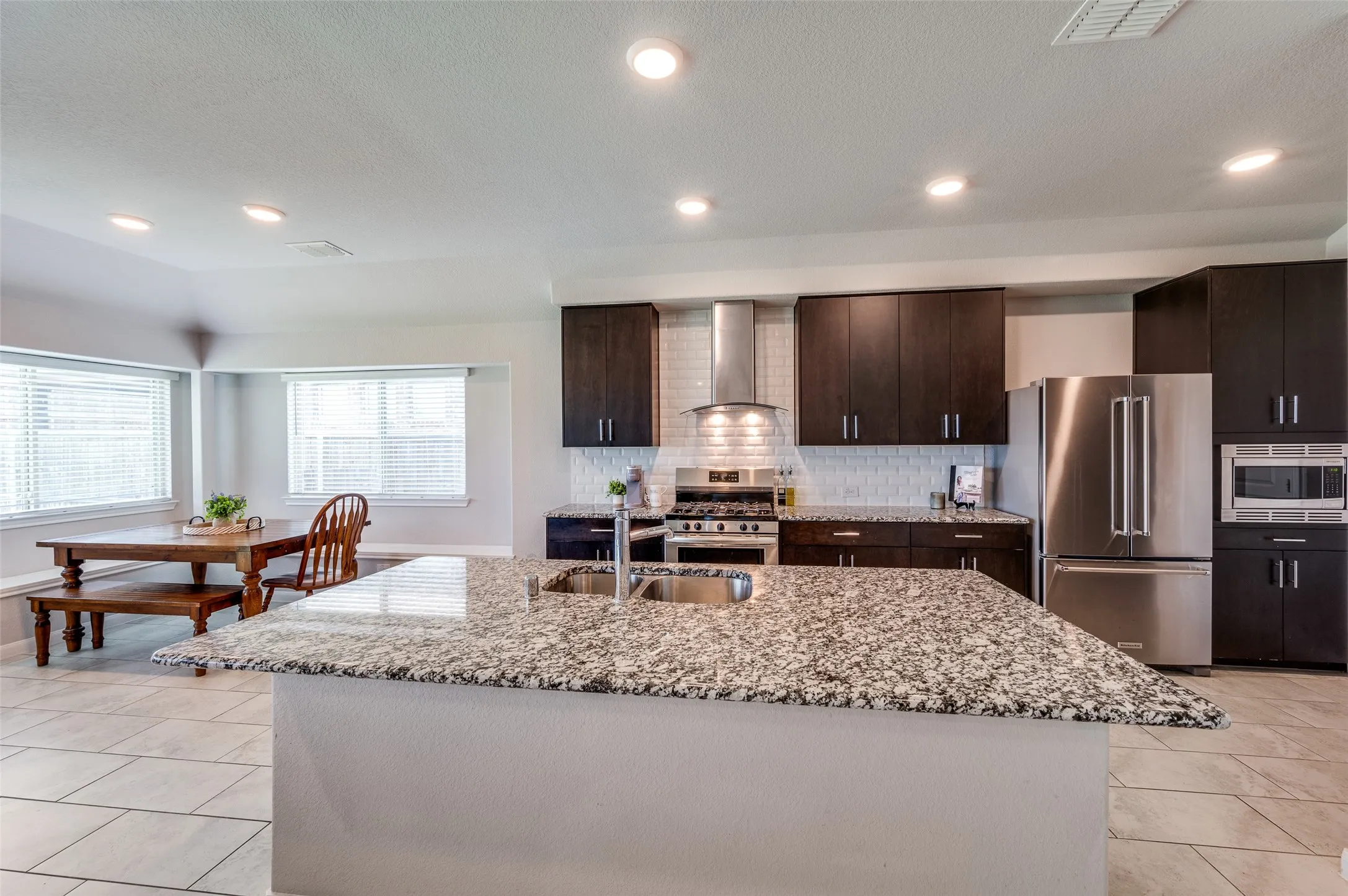 Spacious kitchen featuring an expansive island with an integrated sink, dark wood-finish cabinetry, stainless steel appliances, and recessed lighting