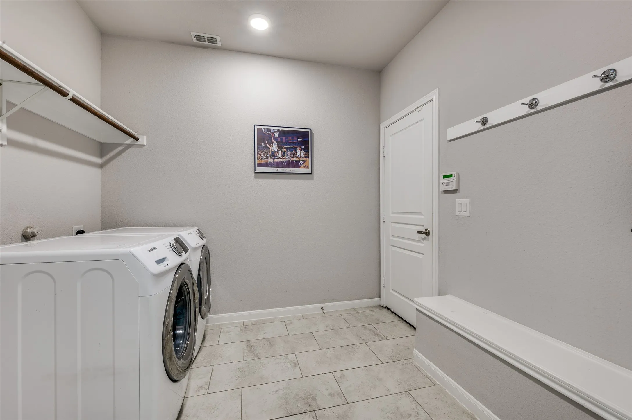 Laundry area featuring light tile flooring, a built-in storage bench, and a wall-mounted coat rack