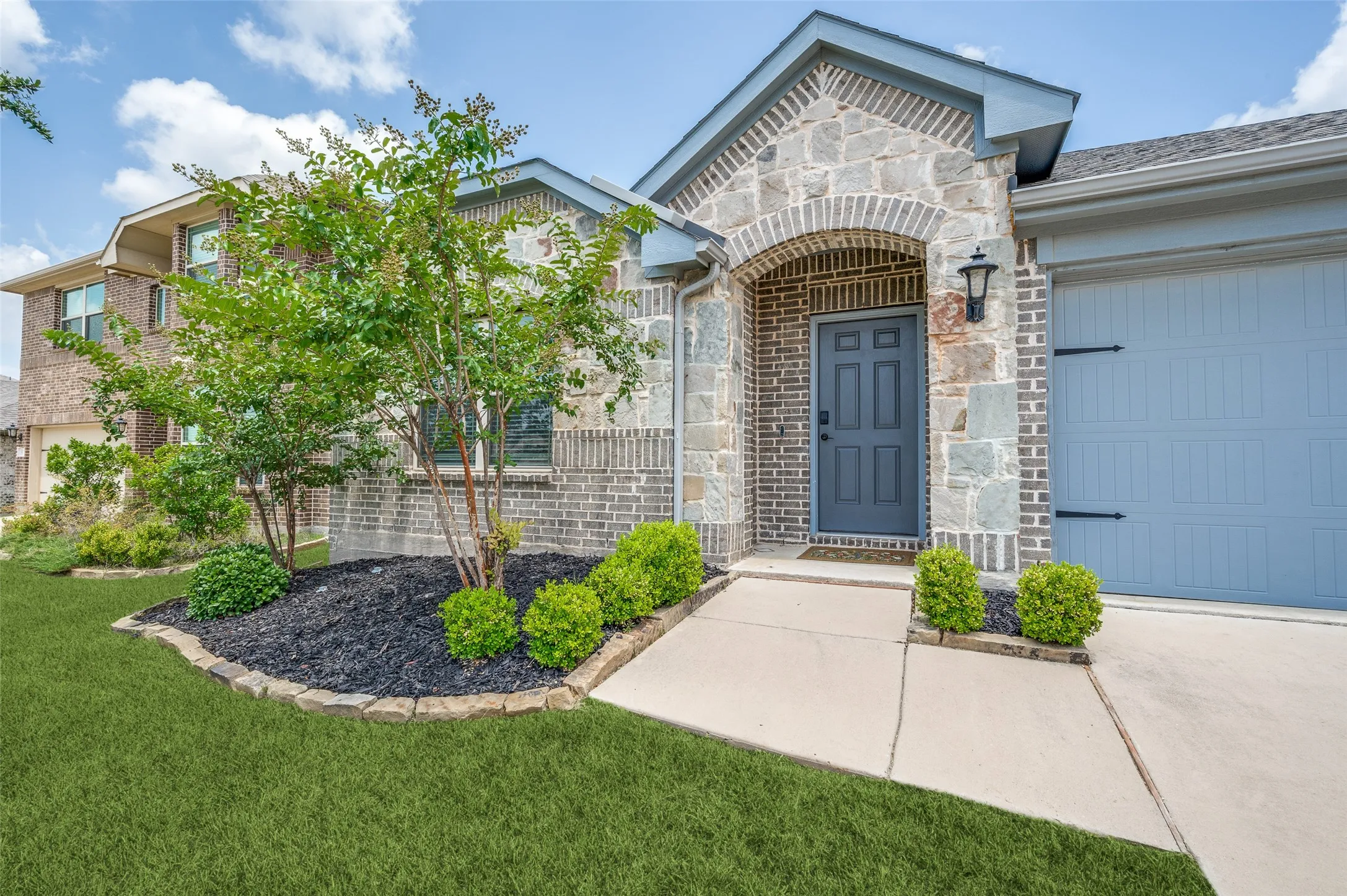 Stone and brick facade with an arched entry, complemented by a garage door with decorative hardware