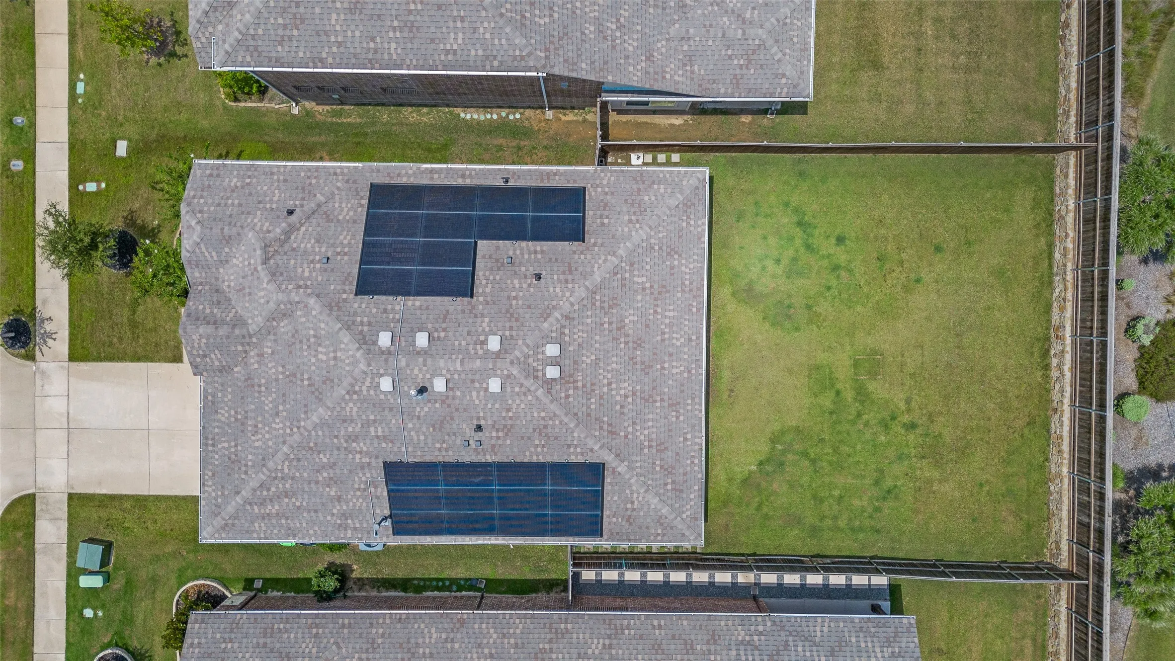 Asphalt shingle roofing with installed solar panels, fenced perimeter, and a grass lawn