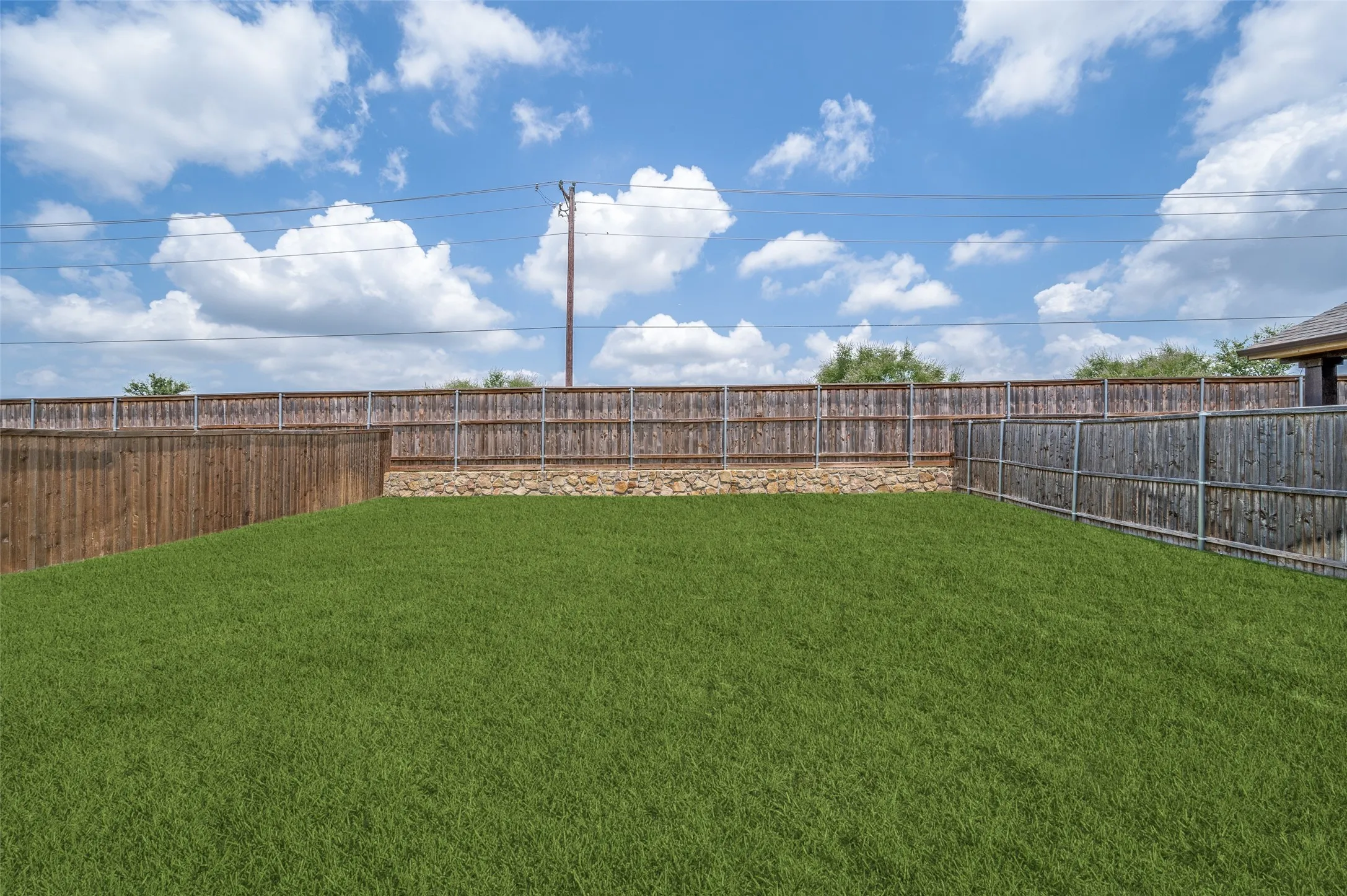 Expansive grassy yard with a wood privacy fence and a stone retaining wall