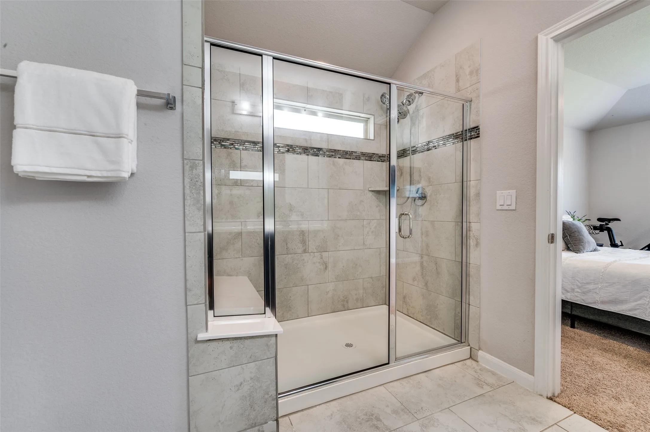 Glass-enclosed shower with a built-in bench, tiled walls, and a decorative accent band