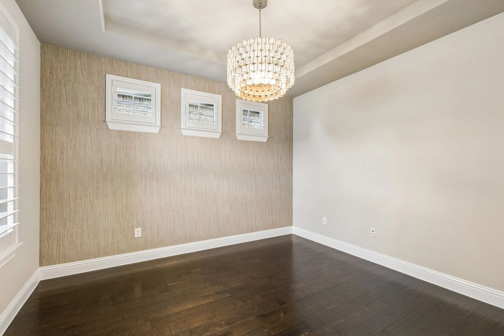 The dedicated home office pairs hardwood floors with a tray ceiling, grasscloth wallpaper accent wall and statement designer chandelier.