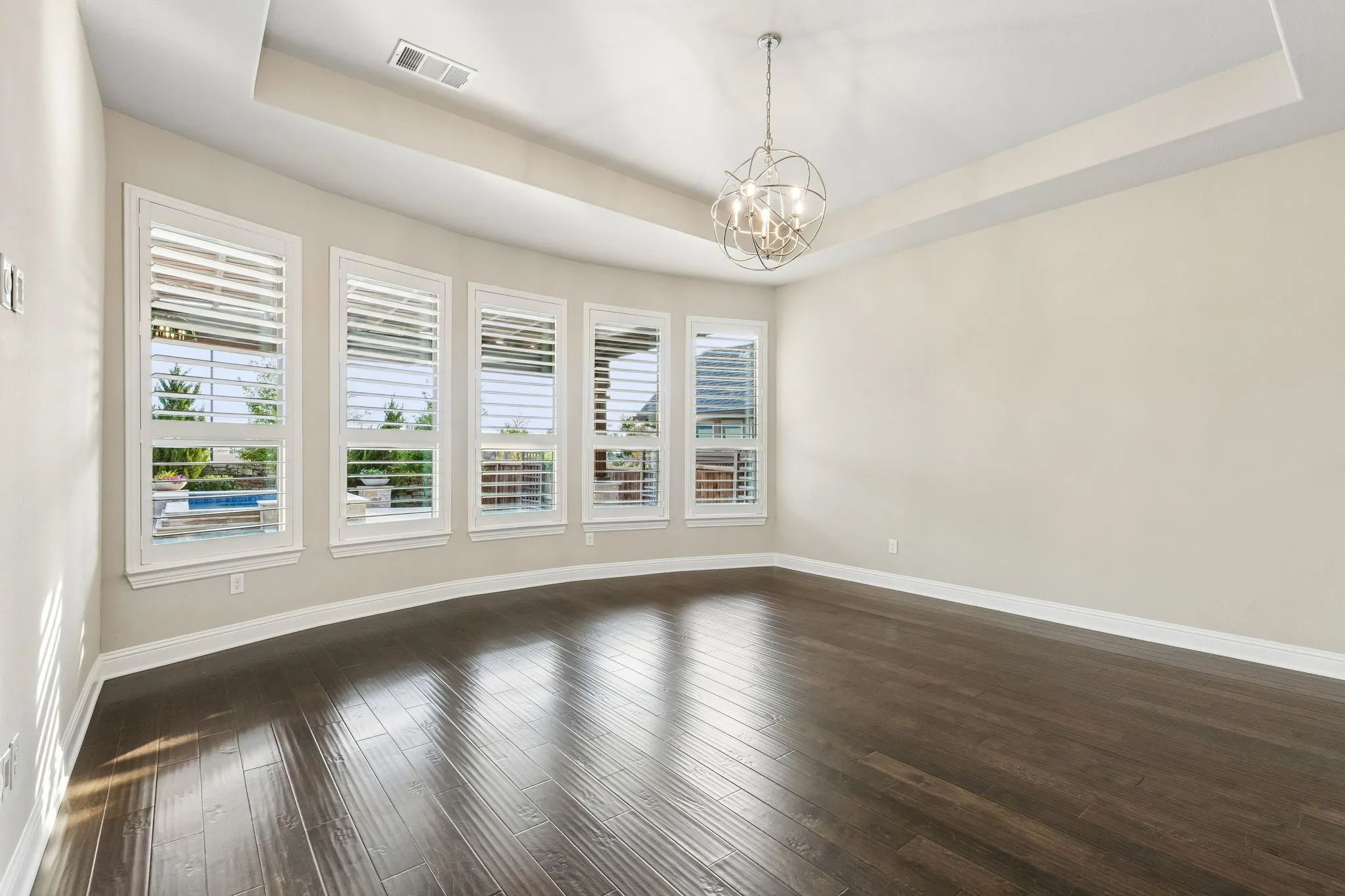 A bowed wall of plantation-shuttered windows fills the primary suite with natural light while capturing views toward the backyard and pool.