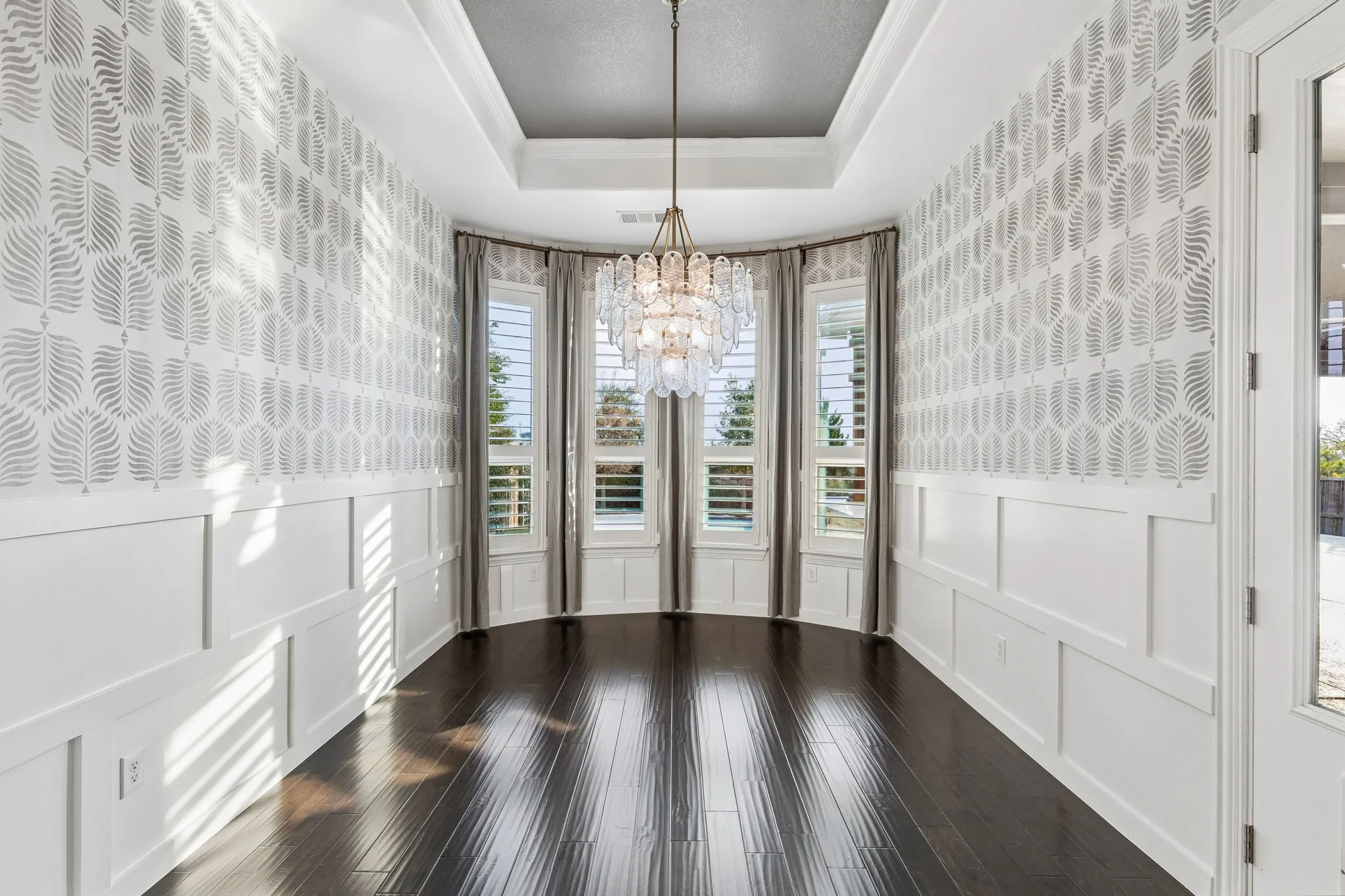 The dedicated dining room makes a statement with board-and-batten wainscoting, Serena & Lily wallpaper, custom drapery and a three-tier glass petal chandelier