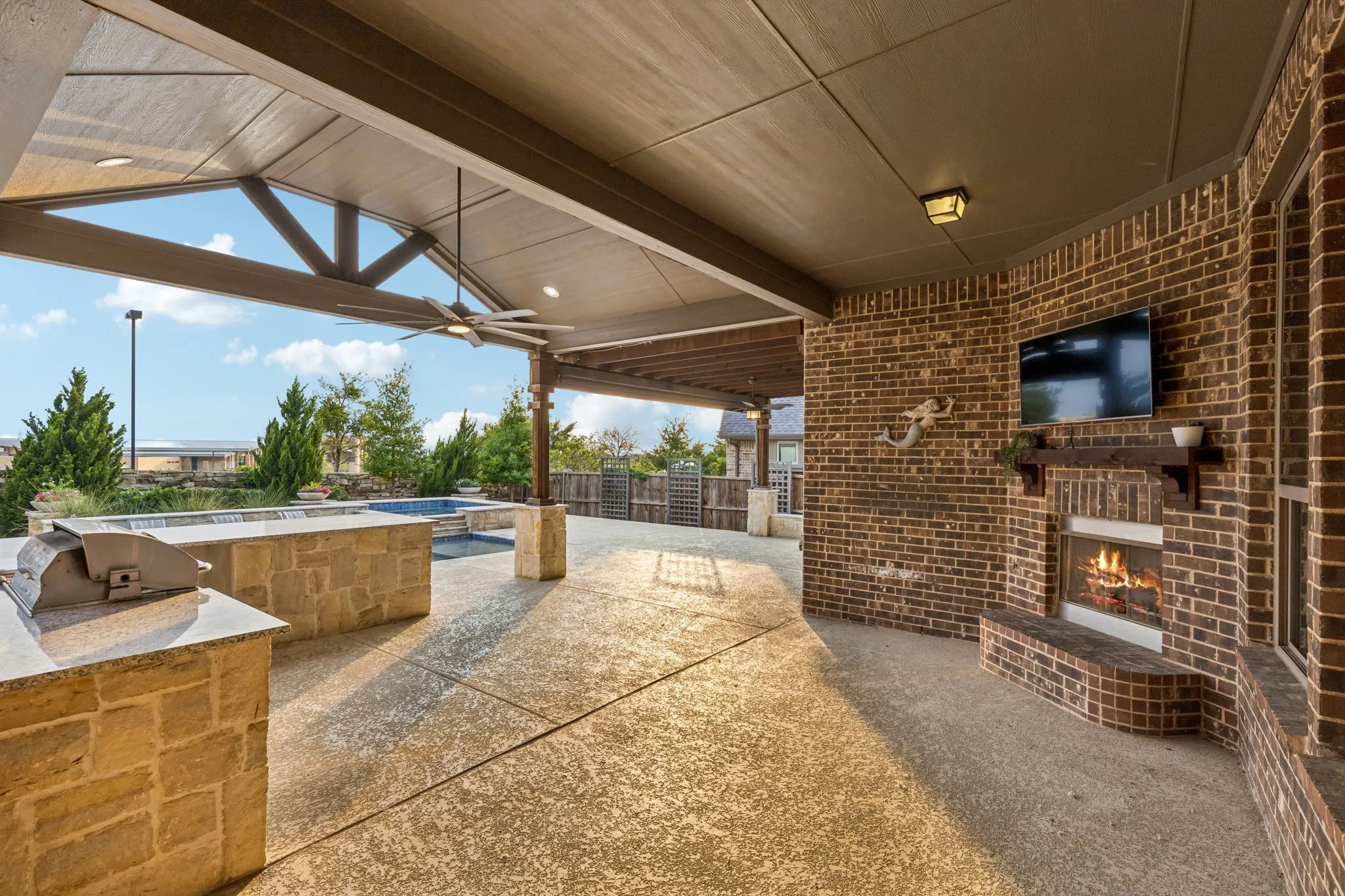 The vaulted extended patio creates a true outdoor living room with a built-in fireplace, TV and seamless views toward the pool.
