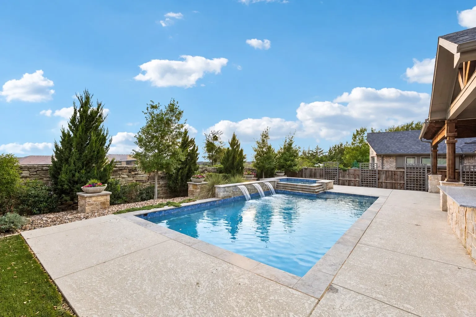 The heated saltwater pool & spa is set against professionally curated landscaping with river rock, planter-topped pillars, trellises and layered greenery