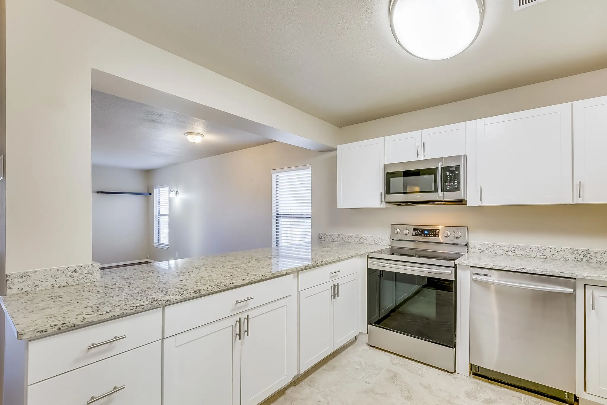 Kitchen with stainless steel appliances, white cabinetry, light stone counters, and a peninsula