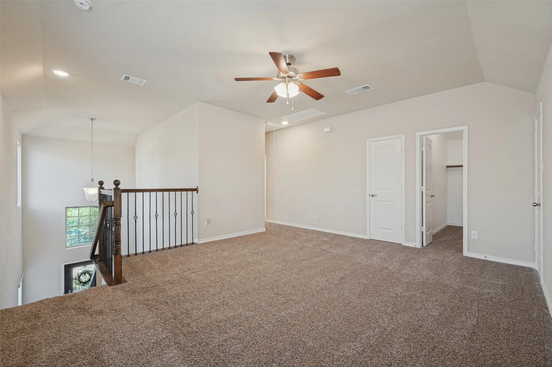 Expansive carpeted loft space featuring vaulted ceilings, a ceiling fan, recessed lighting, and a wrought iron and wood balustrade