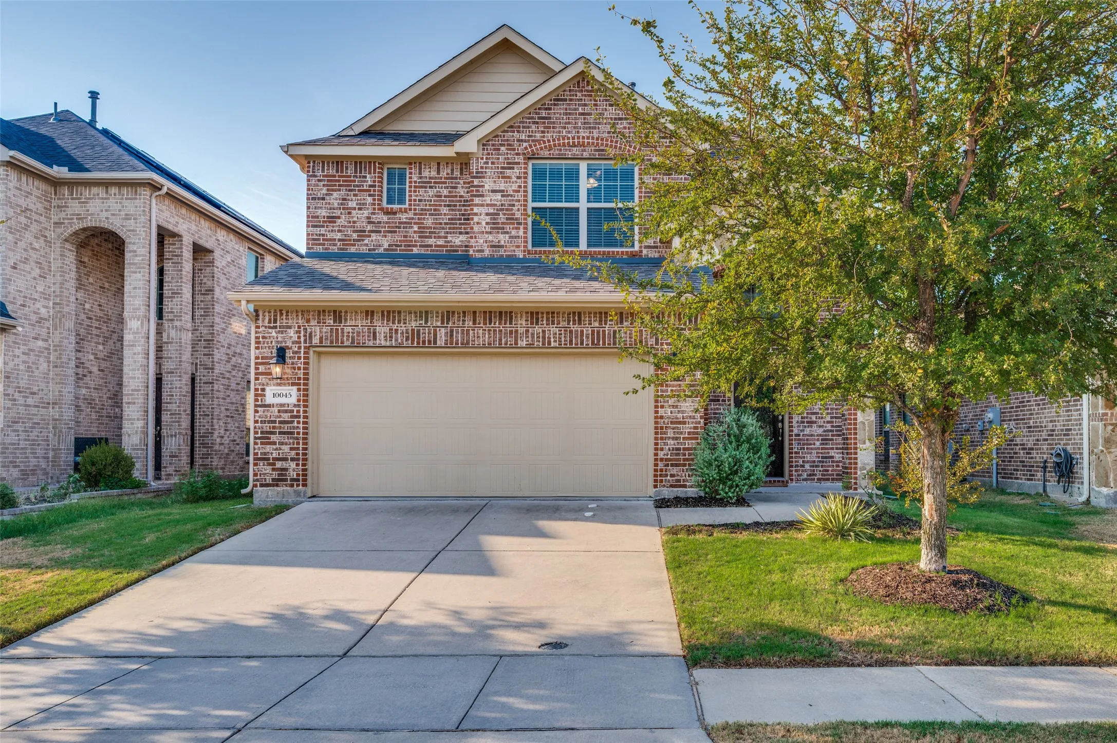 Brick facade with partial stone accents, attached two-car garage, concrete driveway, and established front landscaping
