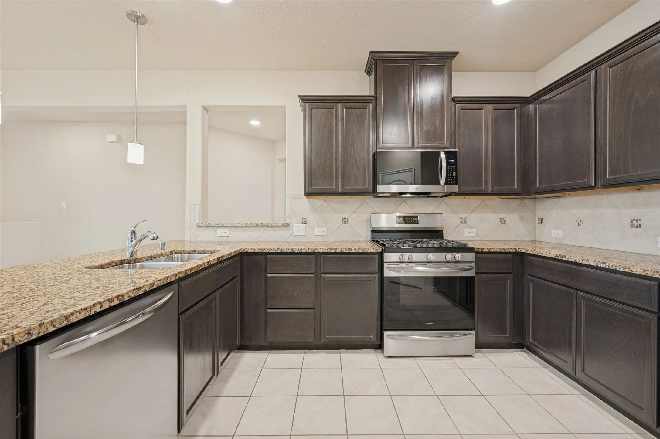 U-shaped kitchen with dark wood cabinetry, light granite countertops, stainless steel appliances, a tile backsplash, and tile flooring