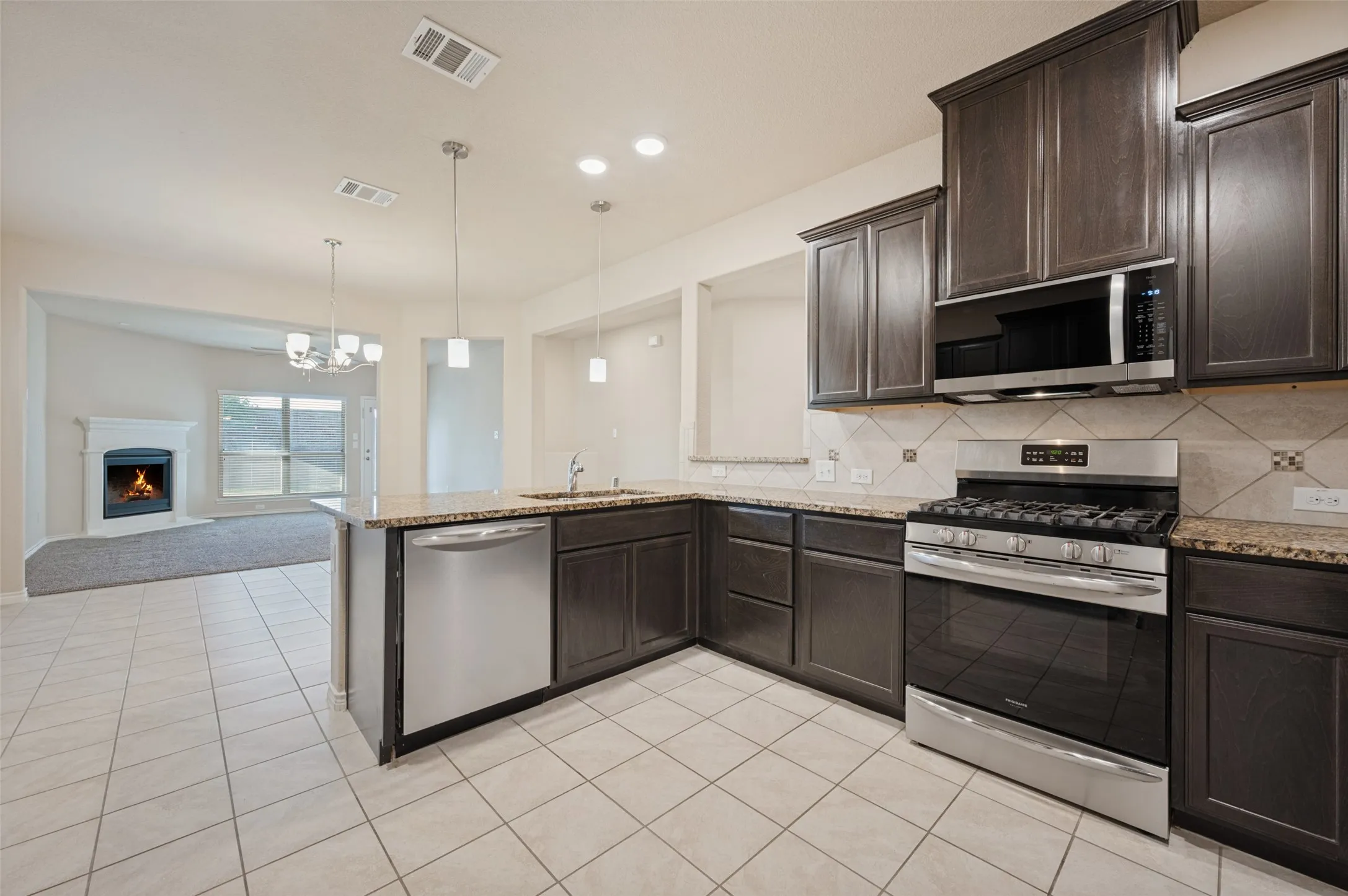 Kitchen featuring dark wood-finish cabinetry, stainless steel appliances, granite countertops, and tile flooring