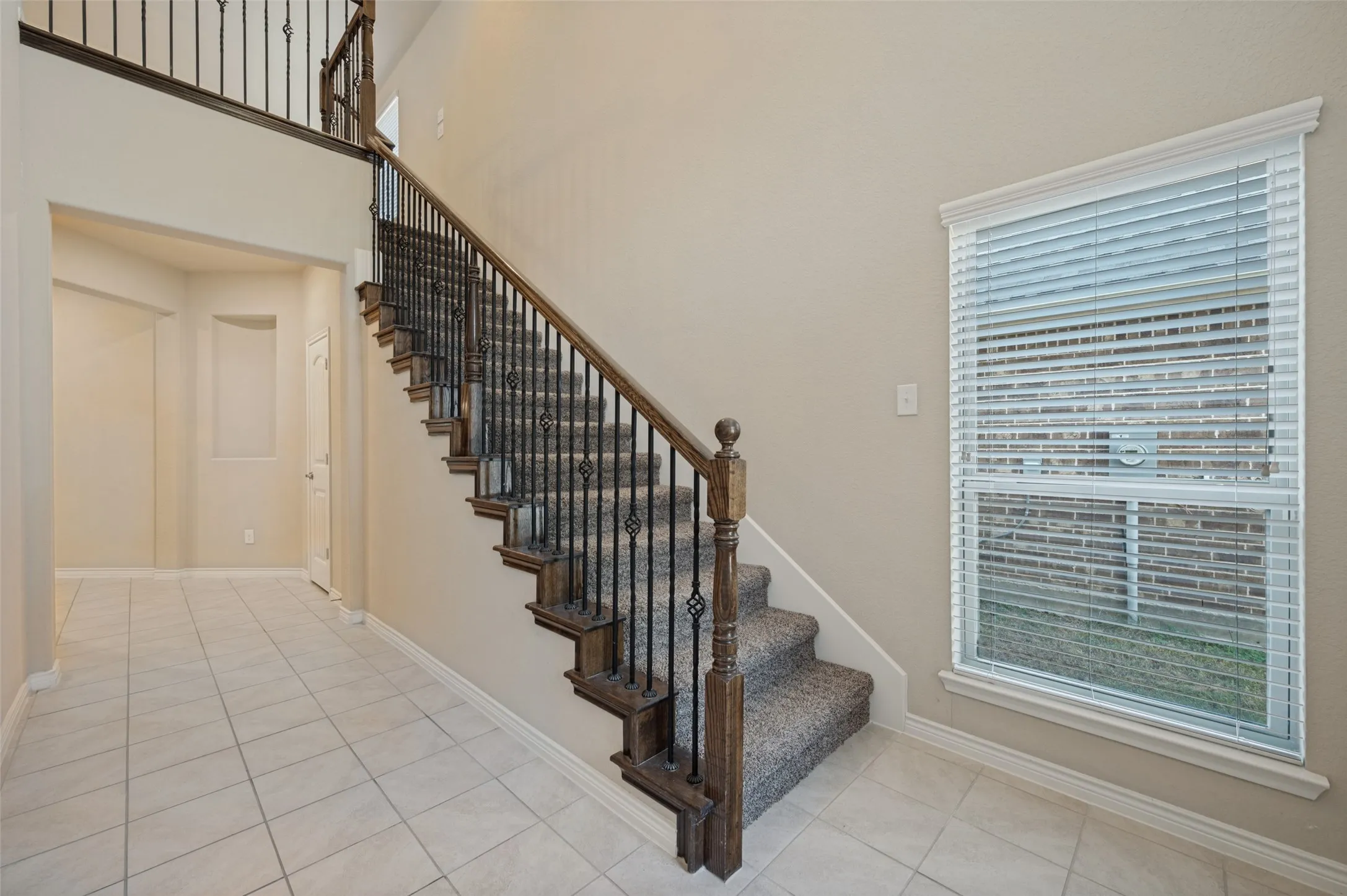 Two-story entryway with tile flooring, staircase featuring iron balusters and wood handrails, and a large window with blinds