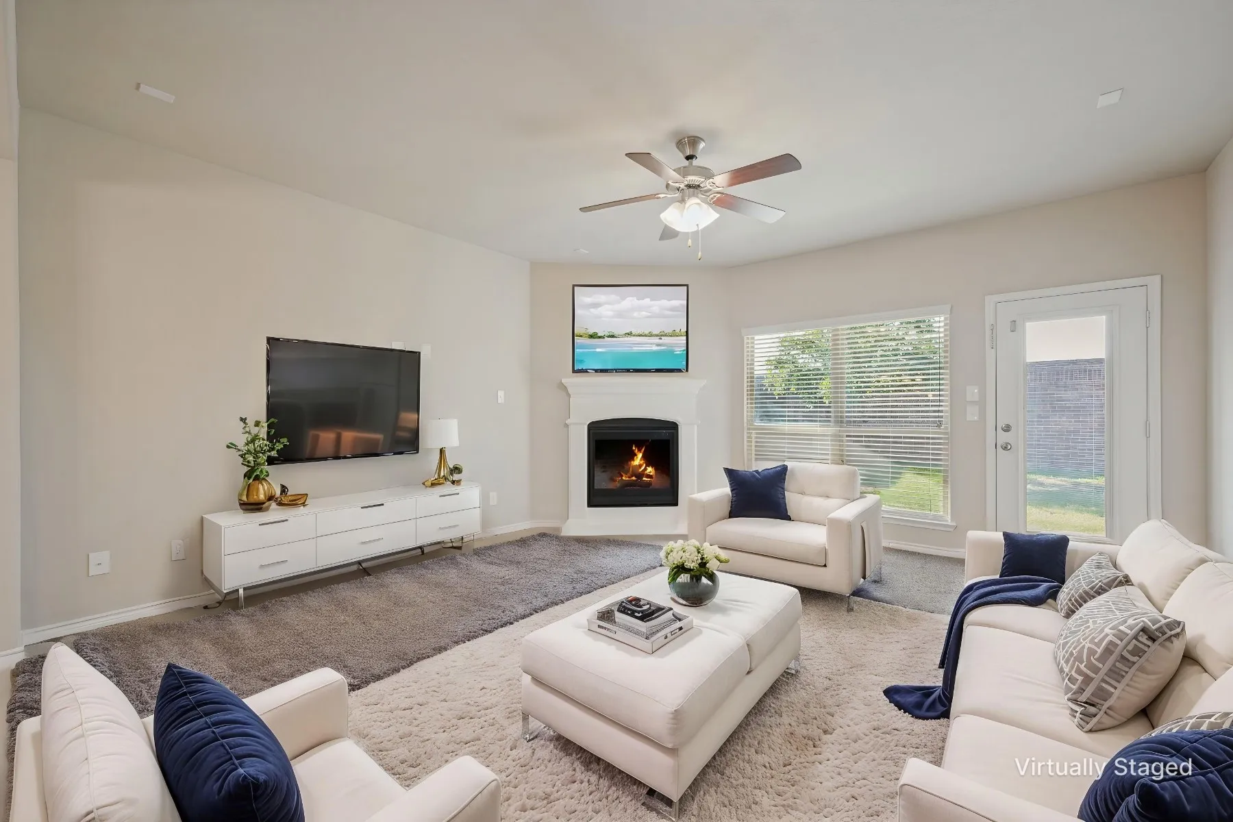 Corner fireplace with a white mantel, ceiling fan with integrated lighting, large window with horizontal blinds, and a glass-paneled door