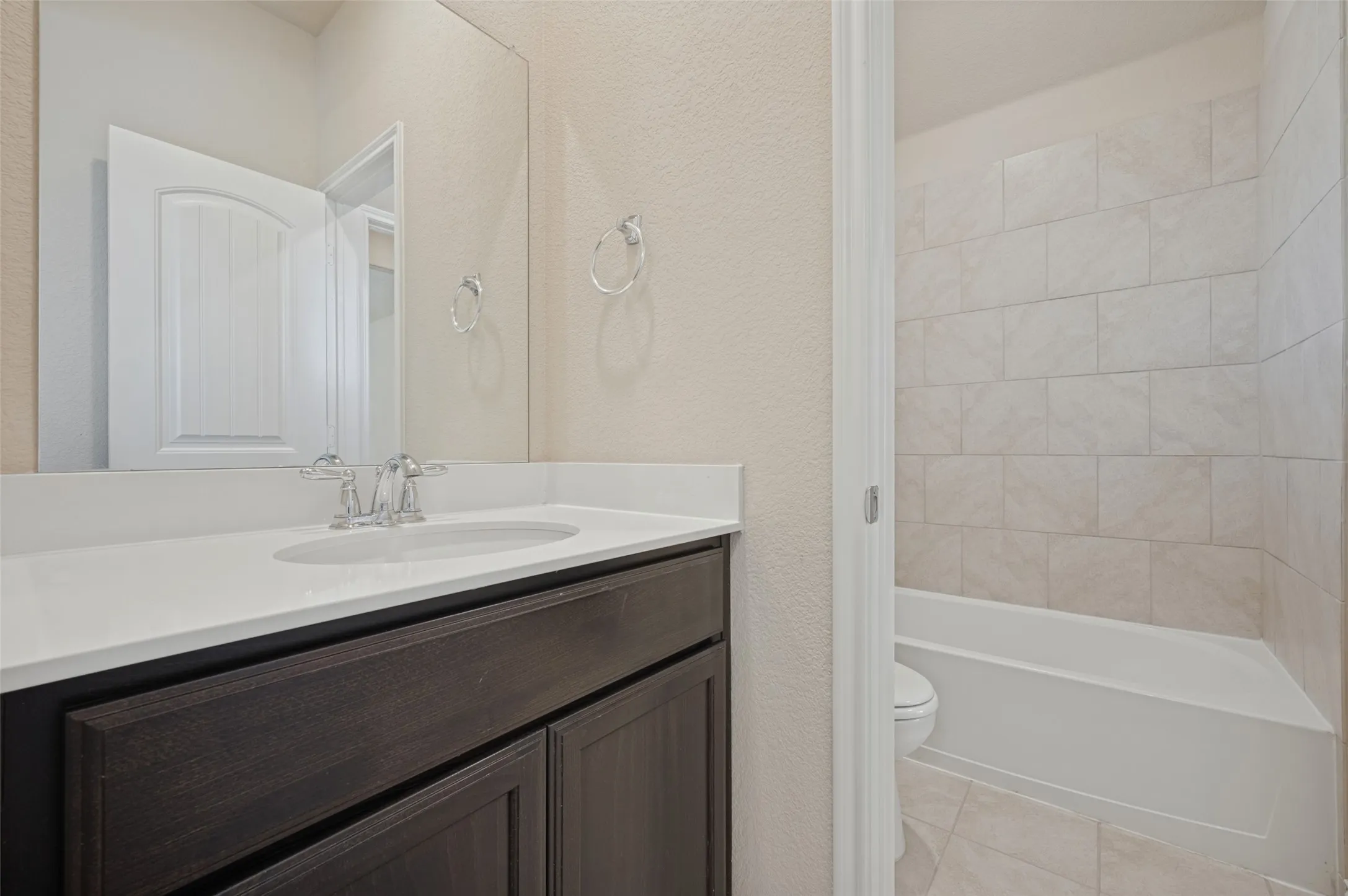 Vanity with a white countertop and undermount sink, chrome faucet, wood-finish cabinetry, and a full-width mirror
