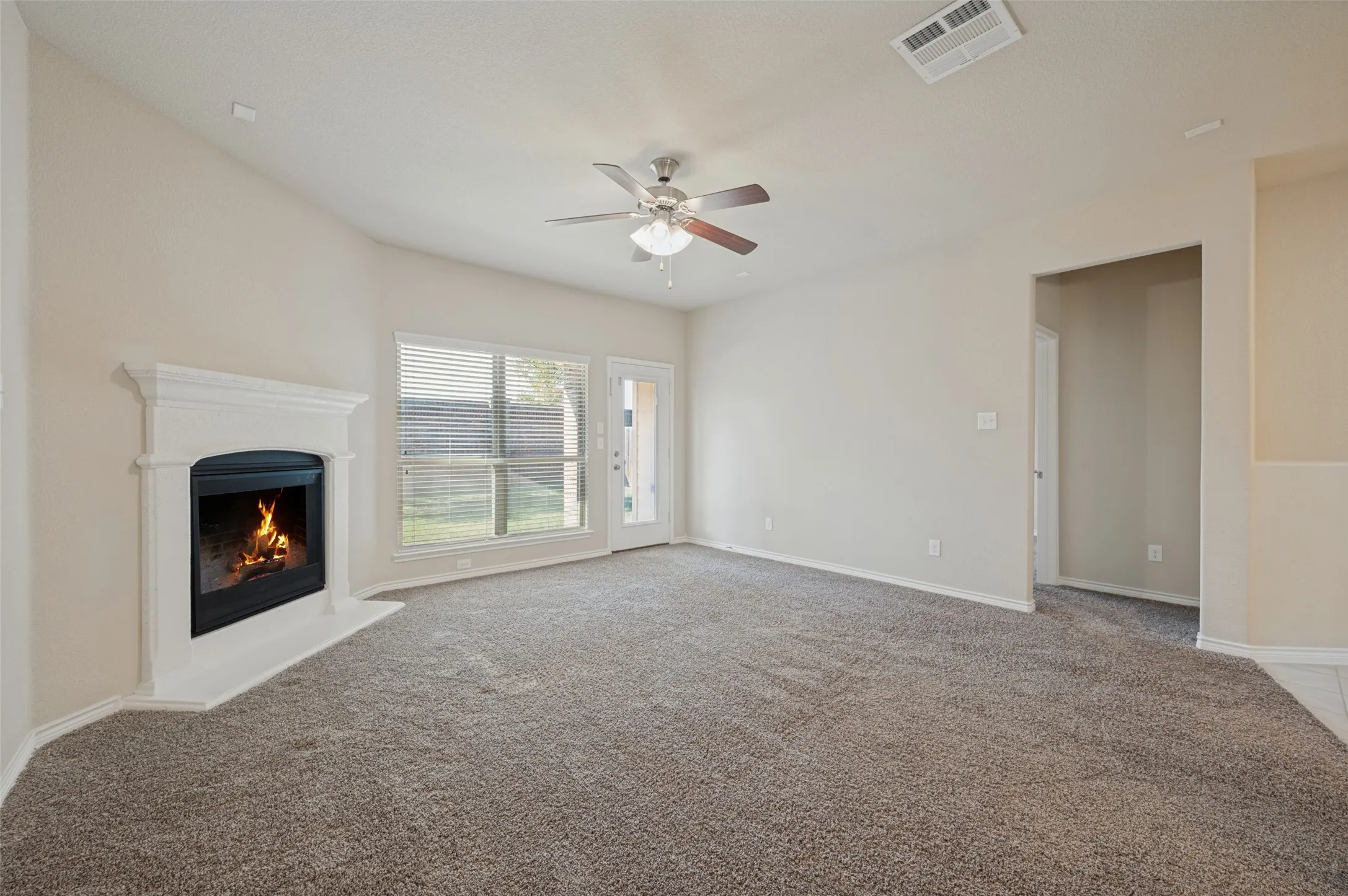 Living area featuring a fireplace with a mantel, a ceiling fan, a window with horizontal blinds, and carpeted flooring