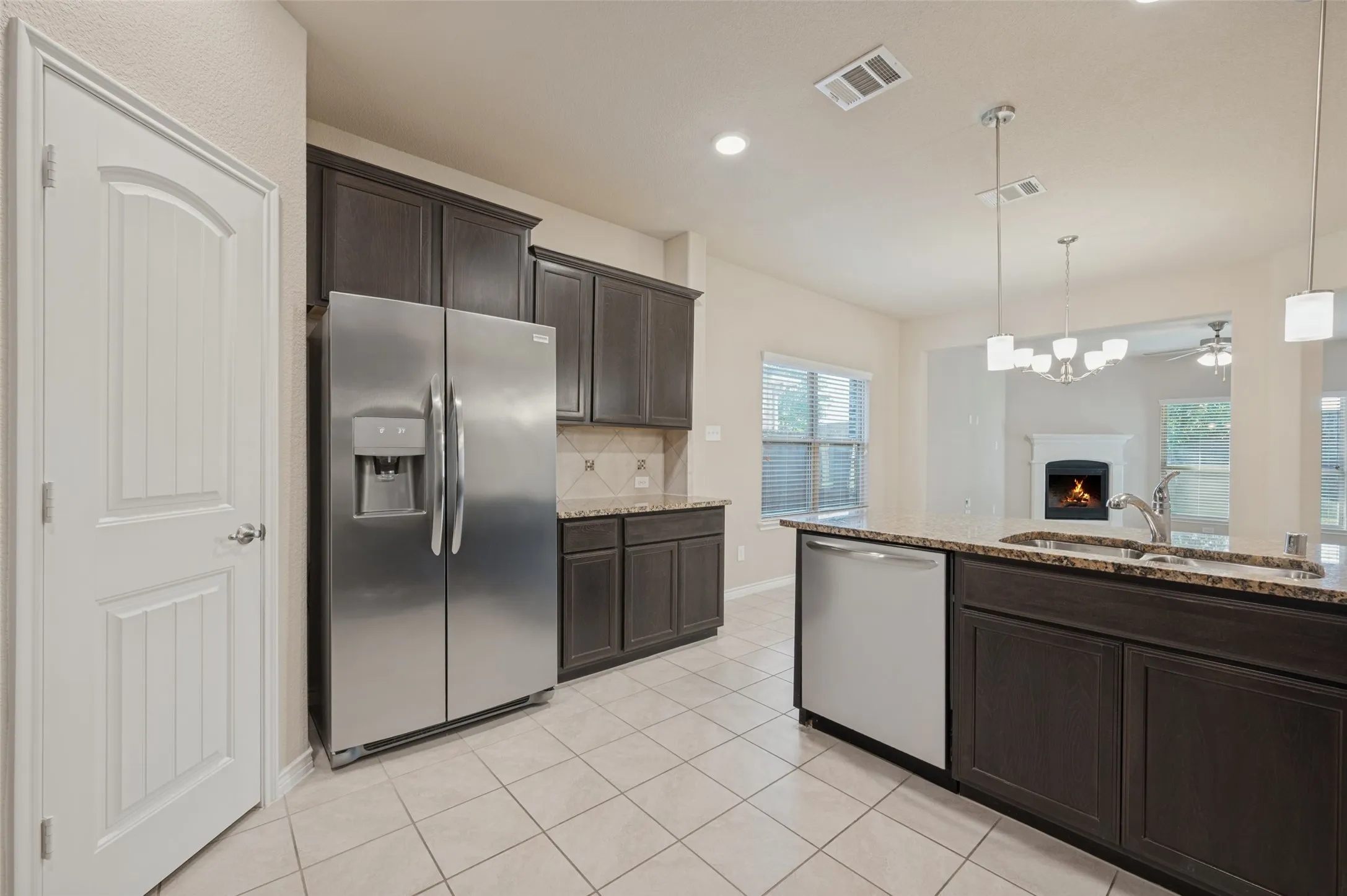 Kitchen featuring tile flooring, dark wood-finish cabinetry, stainless steel appliances, and a central island with a sink