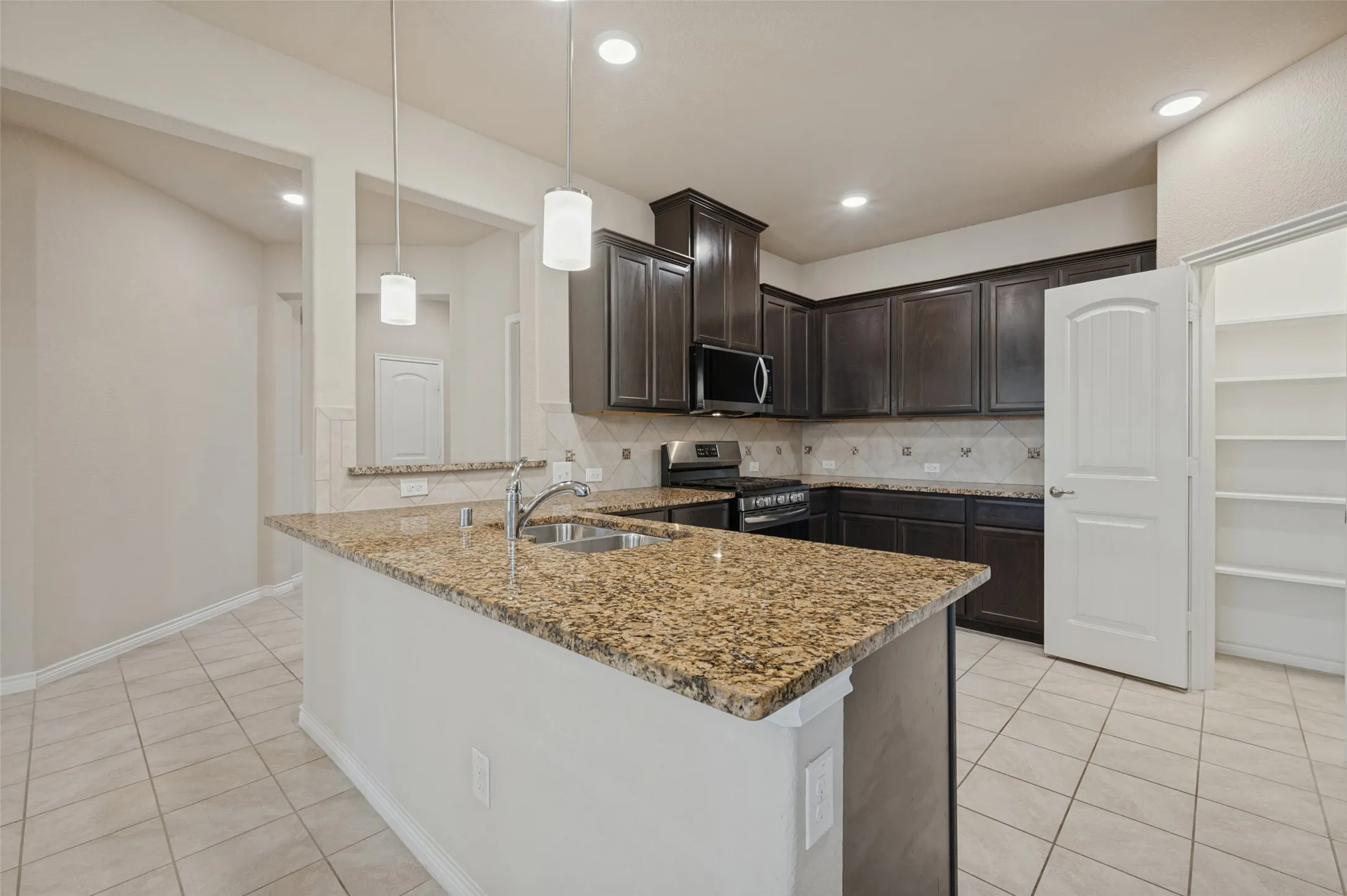 Kitchen island with a stainless steel sink, granite countertops, dark wood cabinetry, and recessed lighting