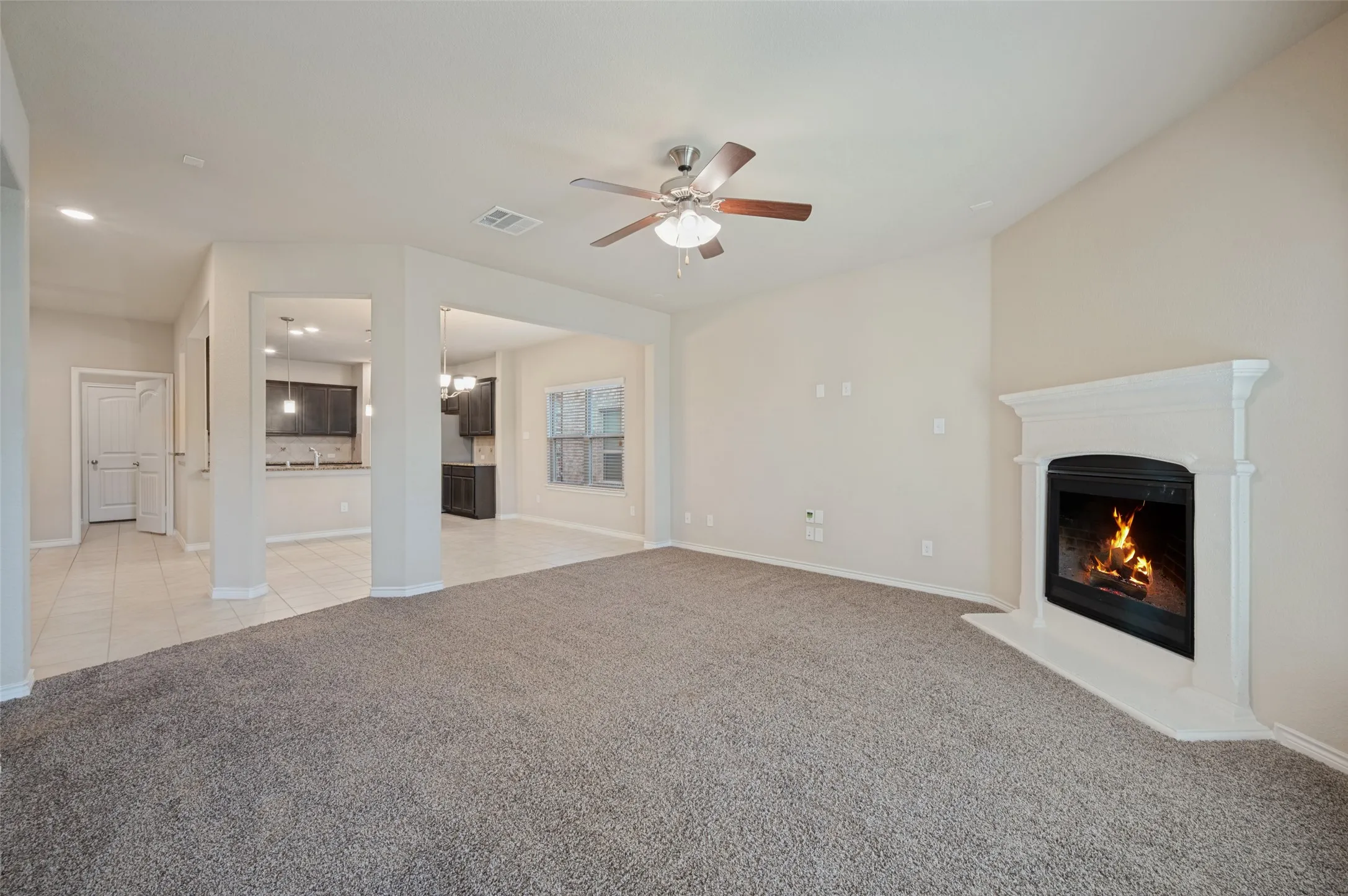 Vaulted ceiling with a ceiling fan, carpeted flooring, fireplace with a white mantel, recessed lighting, and tile flooring in a connected space