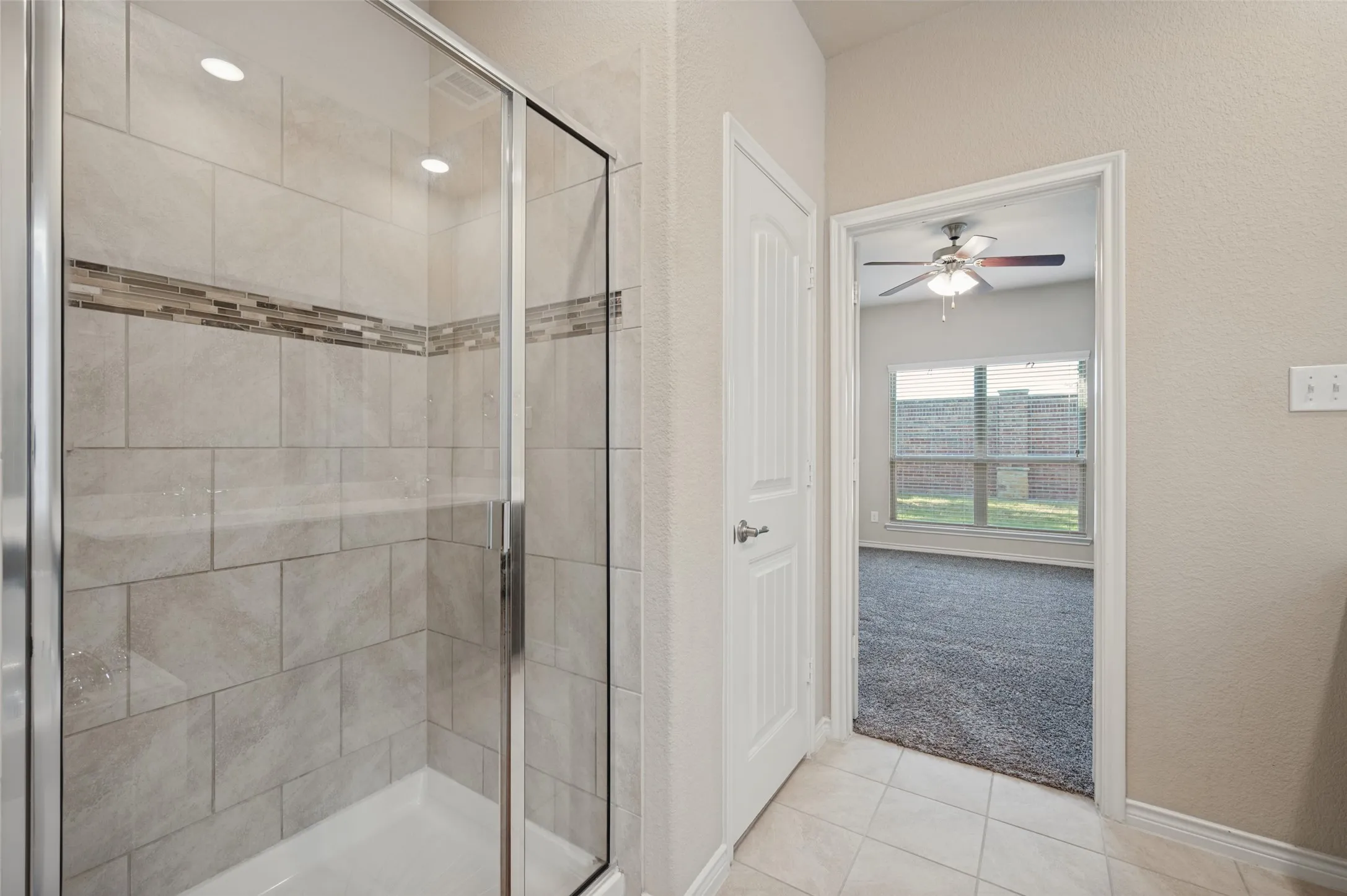 Glass-enclosed shower with subway tile surround and decorative mosaic accent