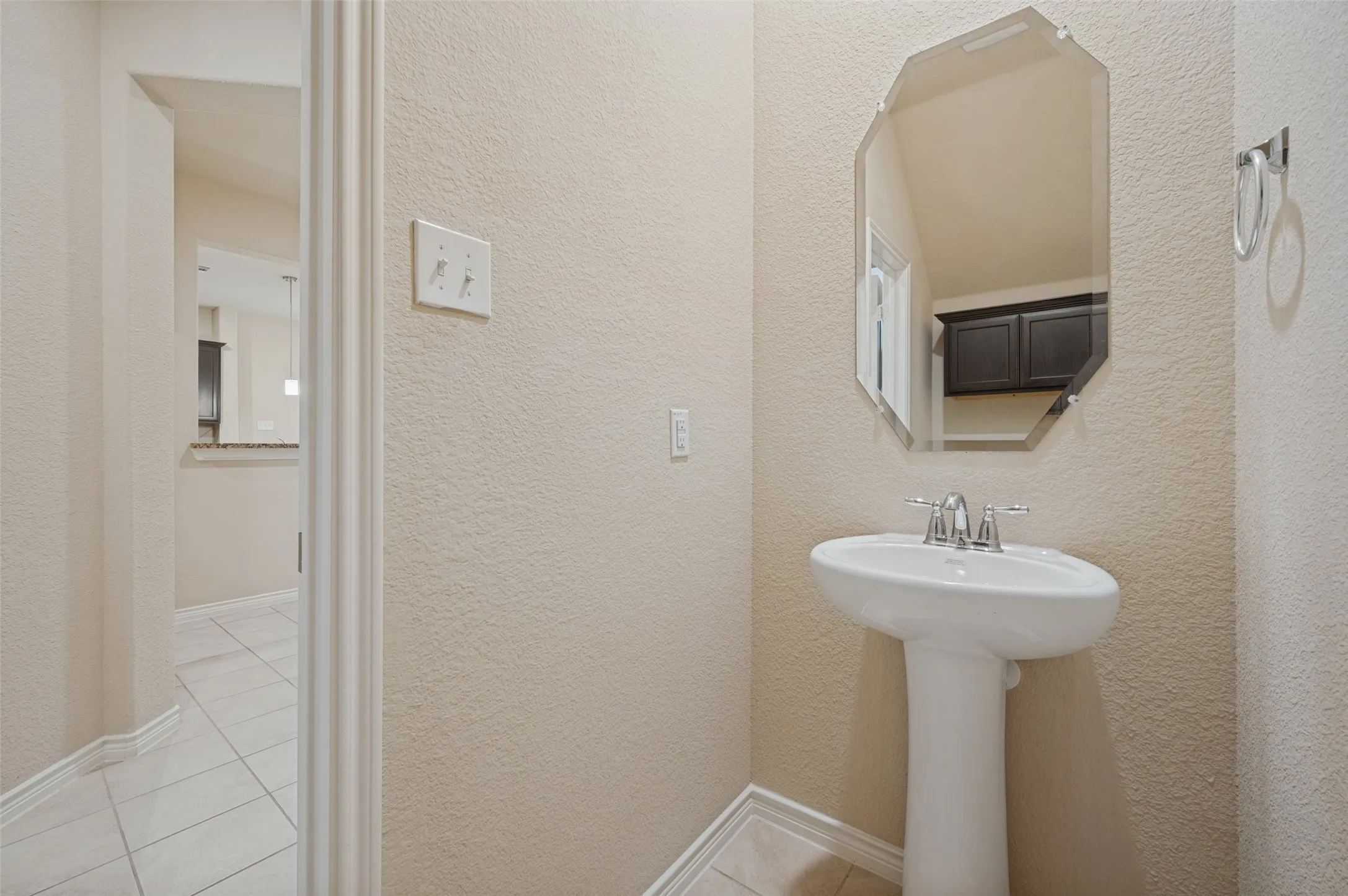 Pedestal sink with chrome faucet, octagonal frameless mirror, and a towel ring