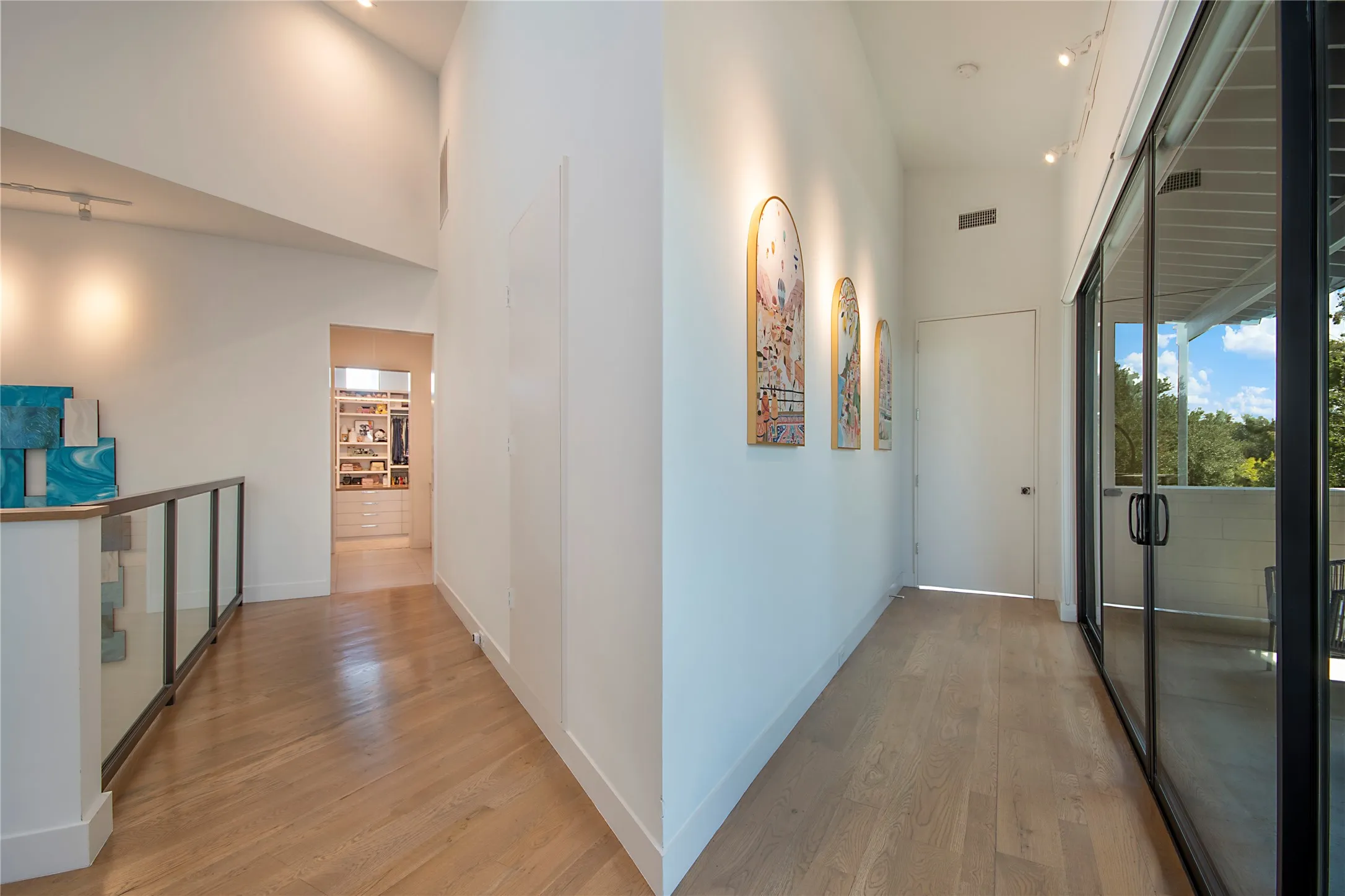 Wood-finish flooring, high ceilings, glass balcony railing, and floor-to-ceiling glass doors opening to an outdoor area
