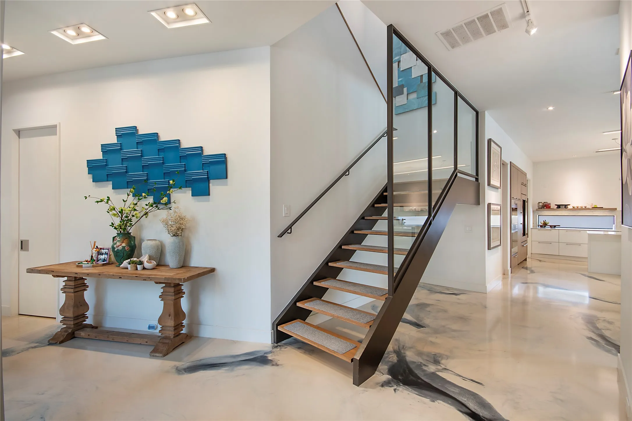 Modern floating staircase with glass railing and wood treads, set against a polished concrete floor with abstract dark accents
