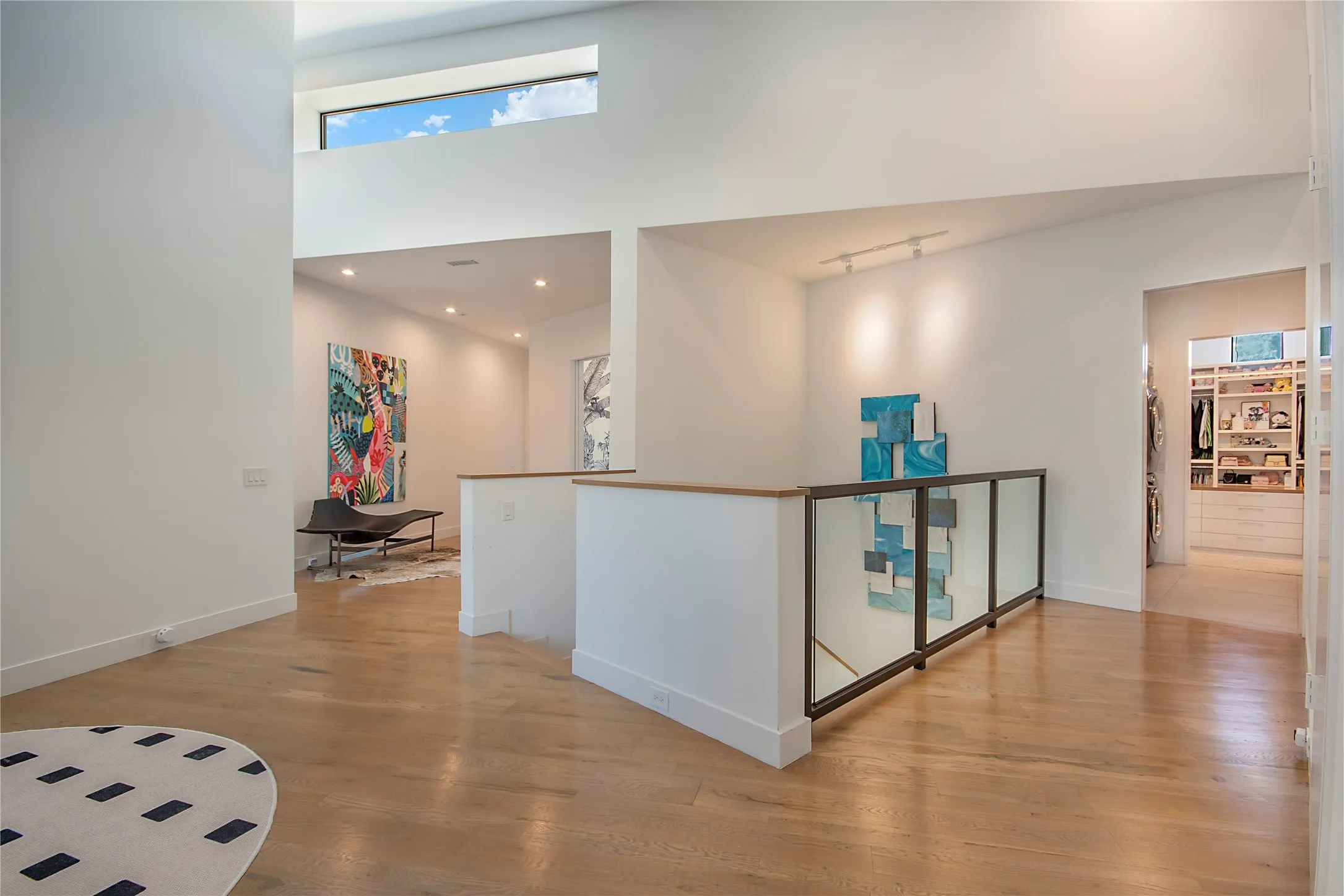 Contemporary gallery-style interior featuring soaring ceilings with clerestory windows, polished wood-finish flooring throughout, and an open floor plan anchored by a central white architectural element with glass panel detailing