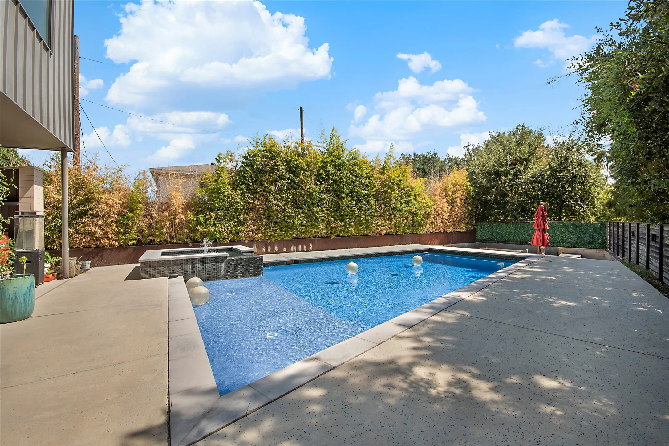 Rectangular swimming pool with integrated spa and water feature, surrounded by concrete decking and privacy landscaping