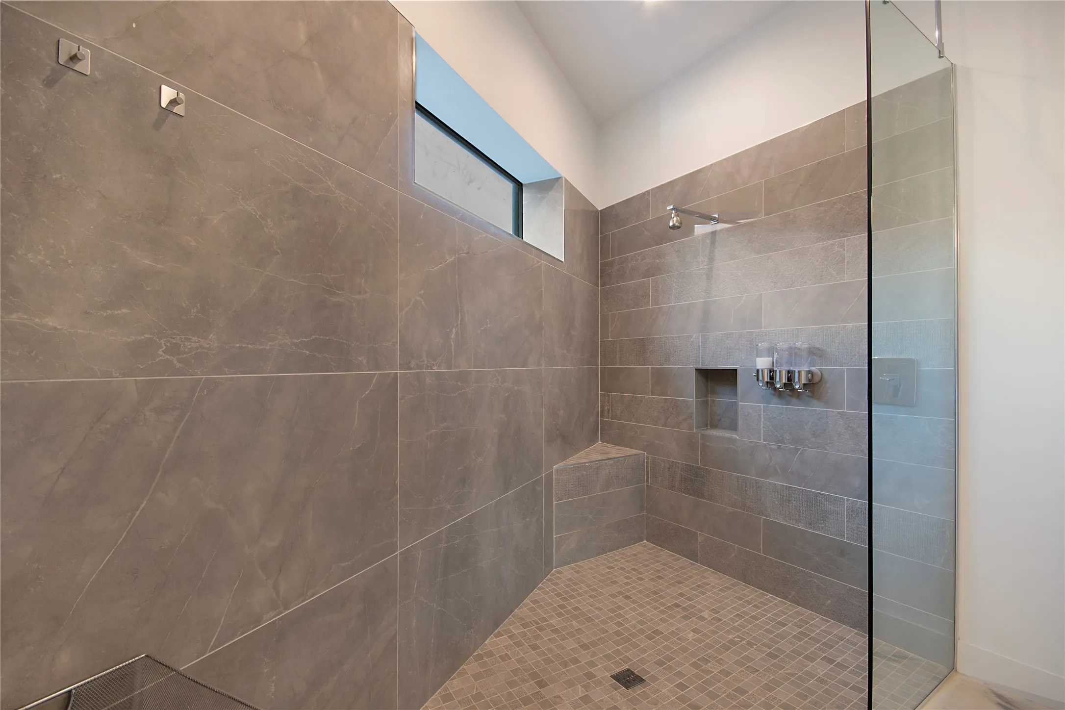 Spacious shower featuring full-height tile, a built-in bench, recessed niche, and a fixed glass panel