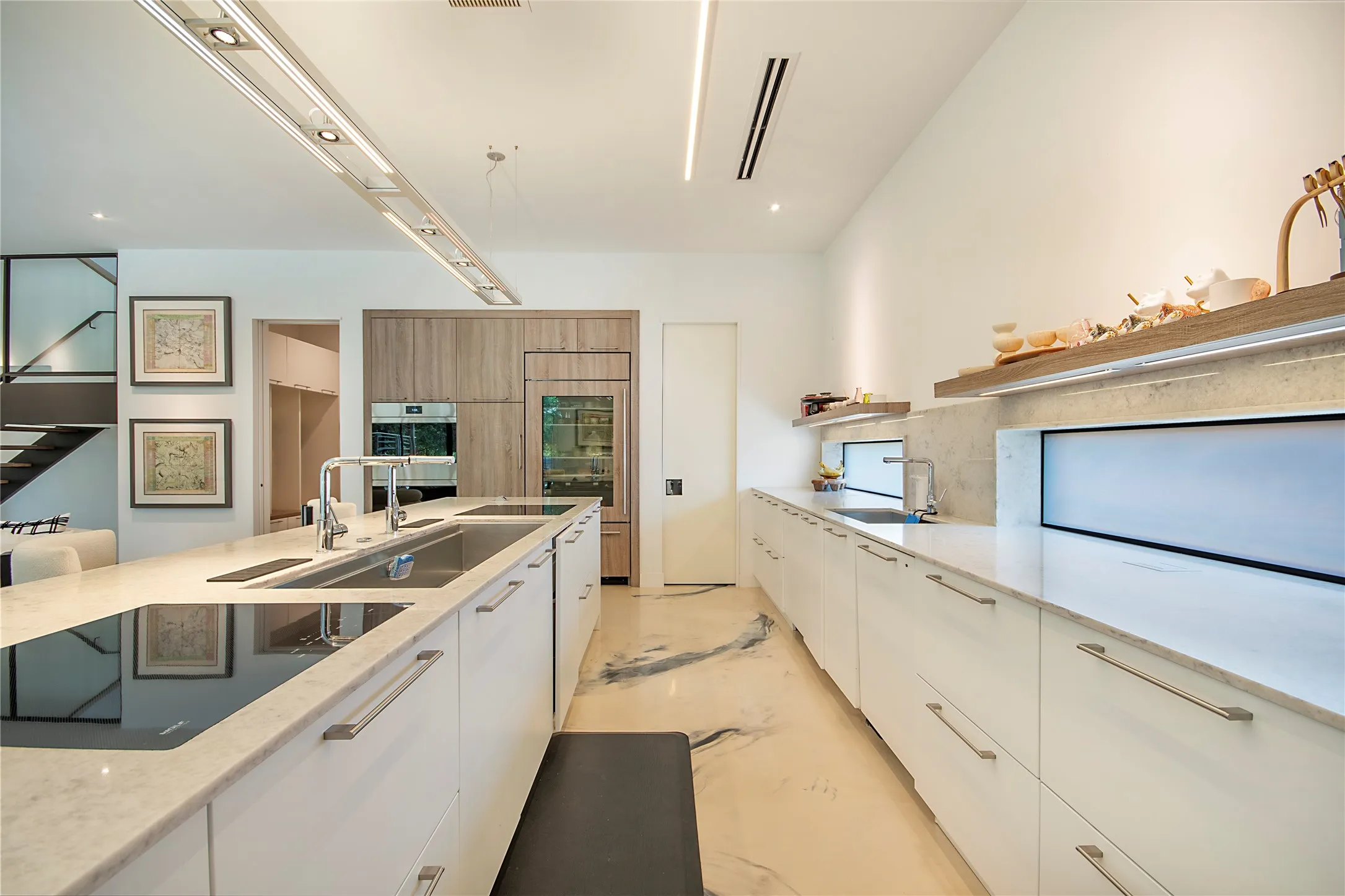Contemporary kitchen featuring white cabinetry, integrated appliances, stone countertops, and an expansive island with an induction cooktop and double sink