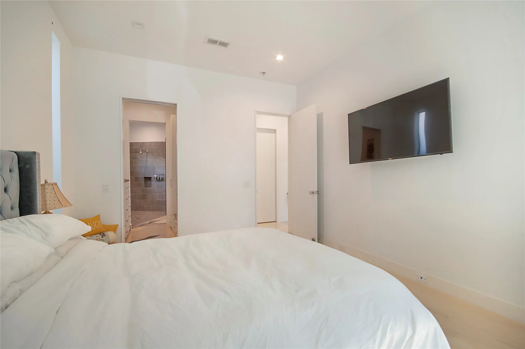 Recessed lighting, wood-finish flooring, and a door leading to a bathroom with a tiled shower