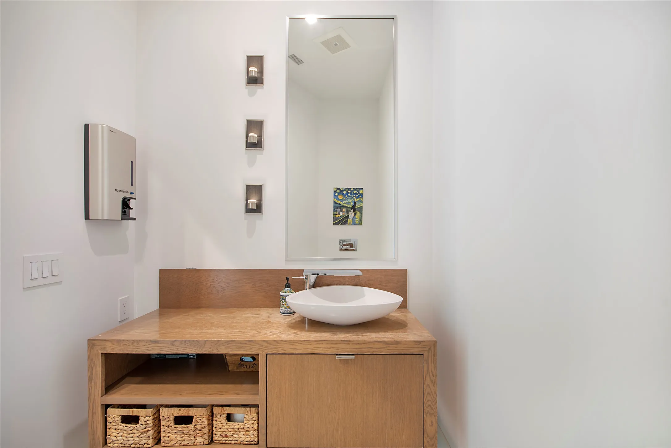 Wood-finish vanity with an integrated vessel sink, framed mirror, and accent sconces