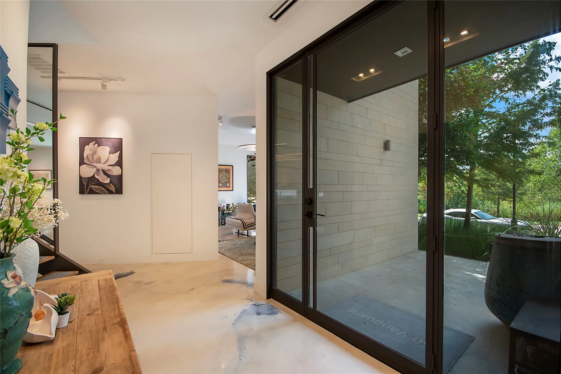 Spacious entryway with light-toned flooring, modern recessed lighting, and a dark-framed glass door
