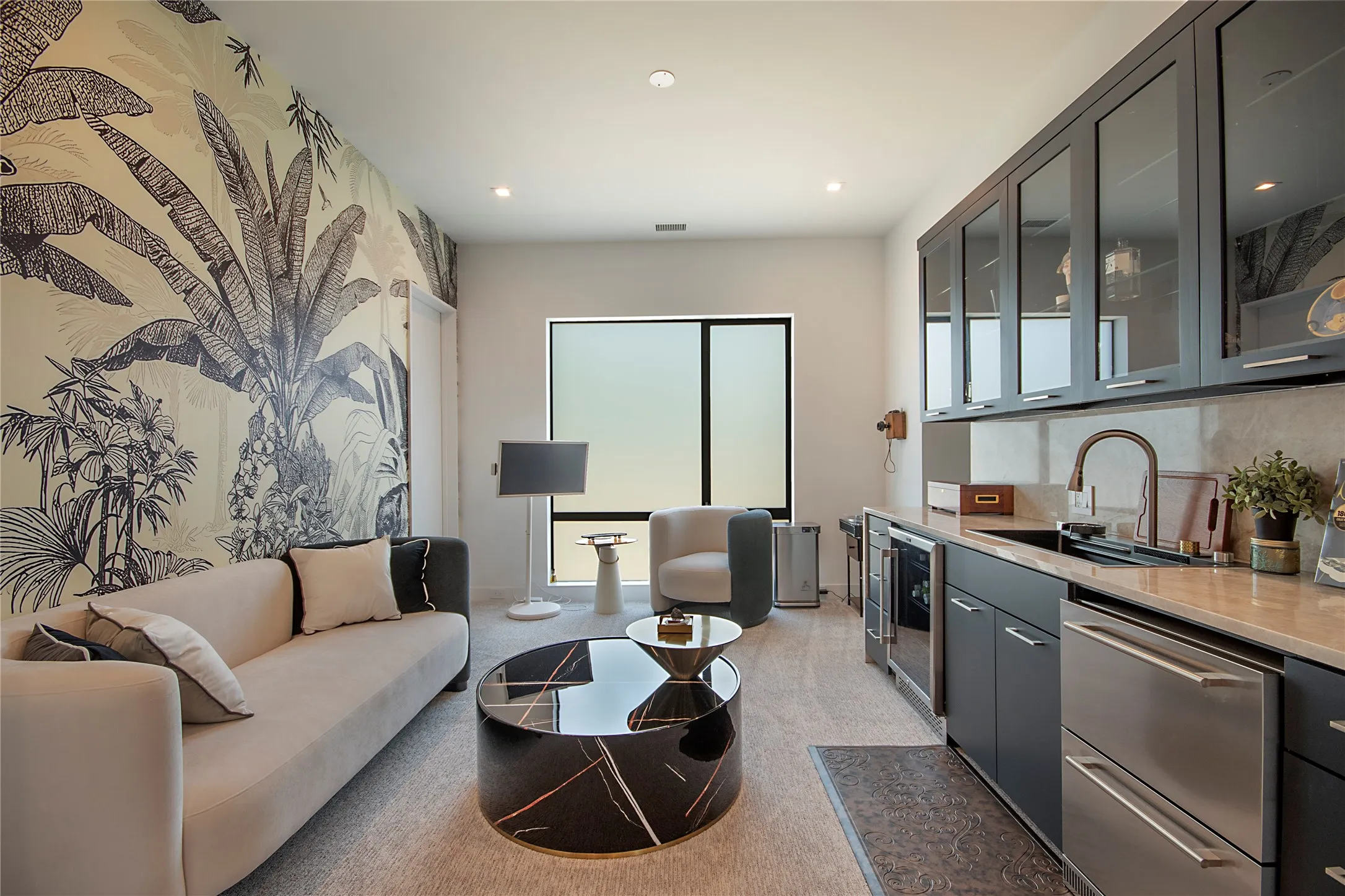 Custom wallpaper accent wall, built-in wet bar with stainless steel appliances, dark cabinetry with glass fronts, recessed lighting, and a large window