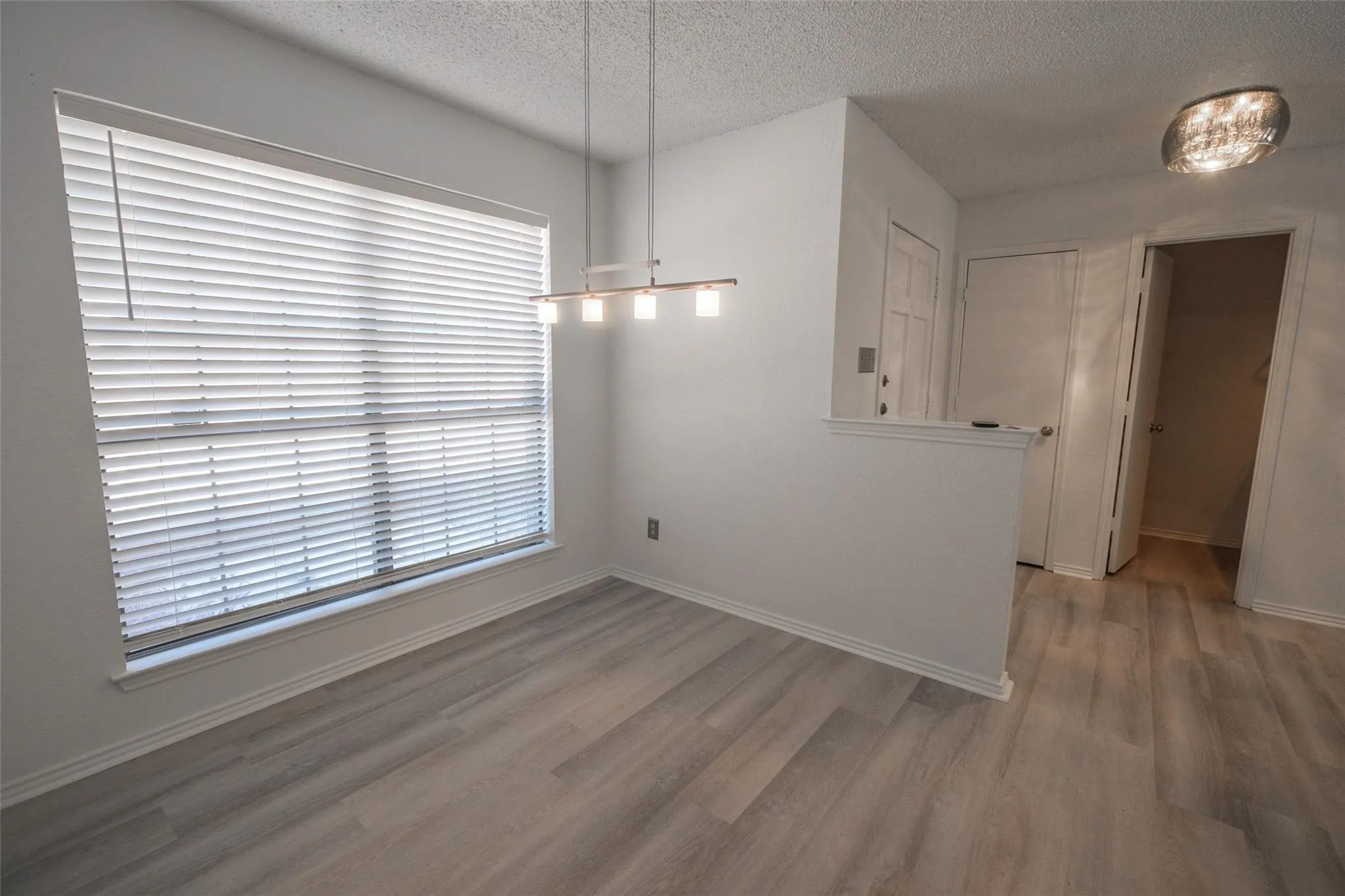 Wood-finish flooring, white horizontal blinds, modern linear pendant light fixture, ceiling-mounted light fixture, white interior doors