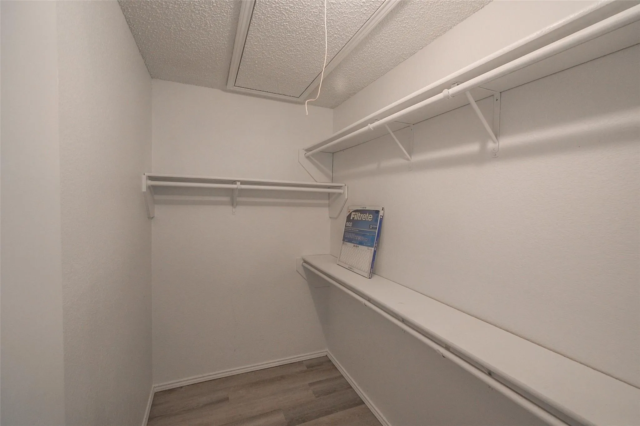Walk-in closet featuring light wood-finish flooring, white walls, and built-in shelving with hanging rods