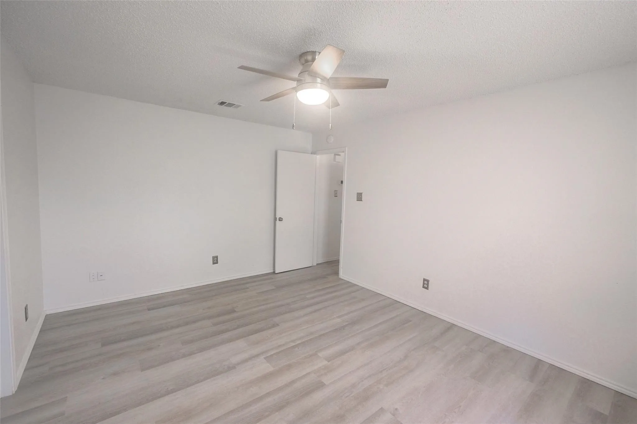 Light wood-finish plank flooring with white walls and a ceiling fan